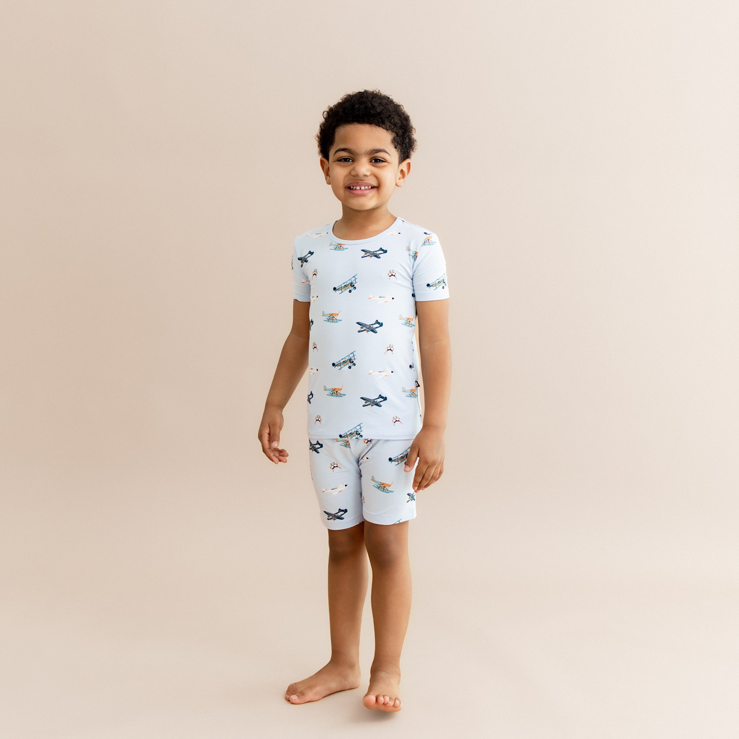 Smiling boy wearing the Short Sleeve Pajamas in Take Off standing in front of a light taupe background