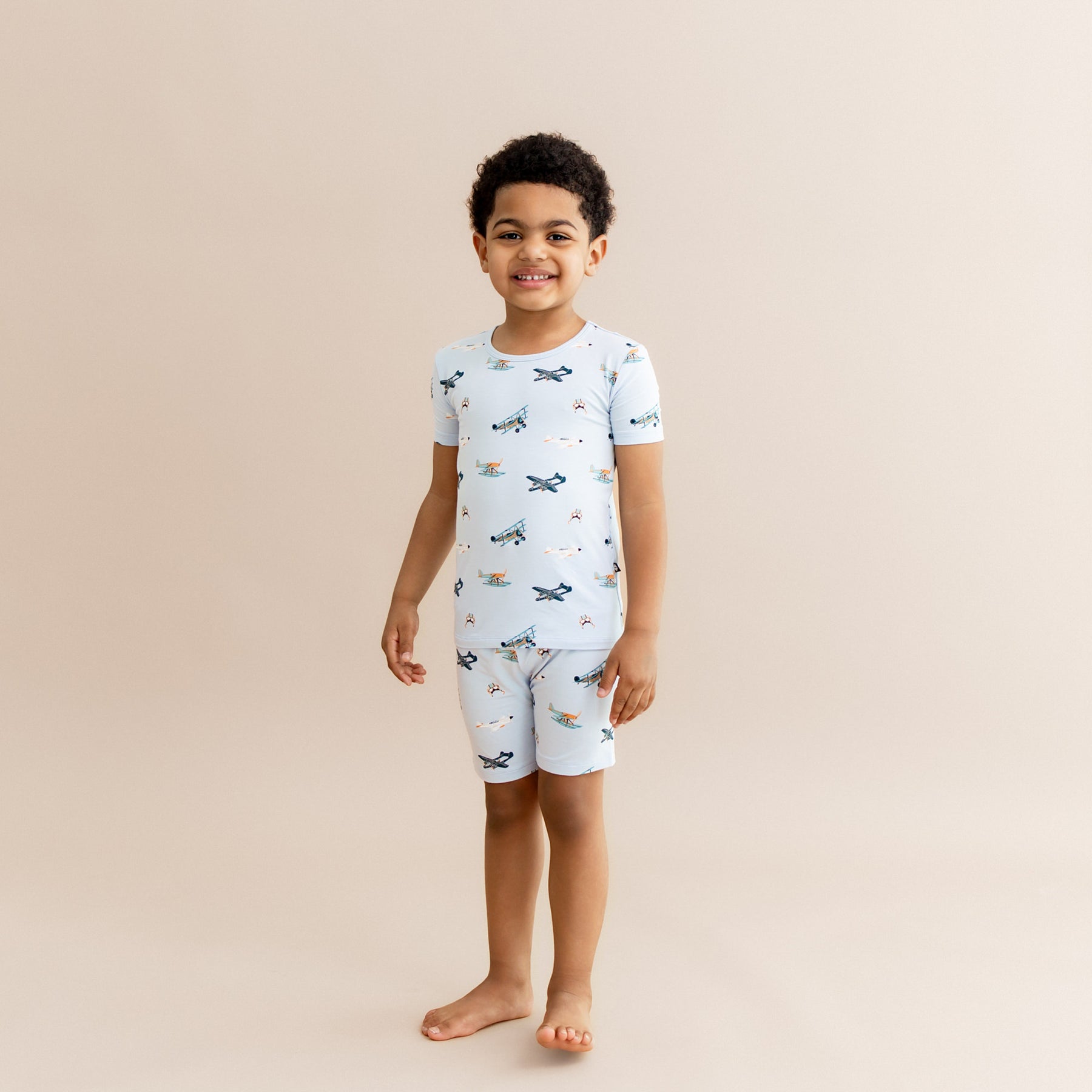 Smiling boy wearing the Short Sleeve Pajamas in Take Off standing in front of a light taupe background