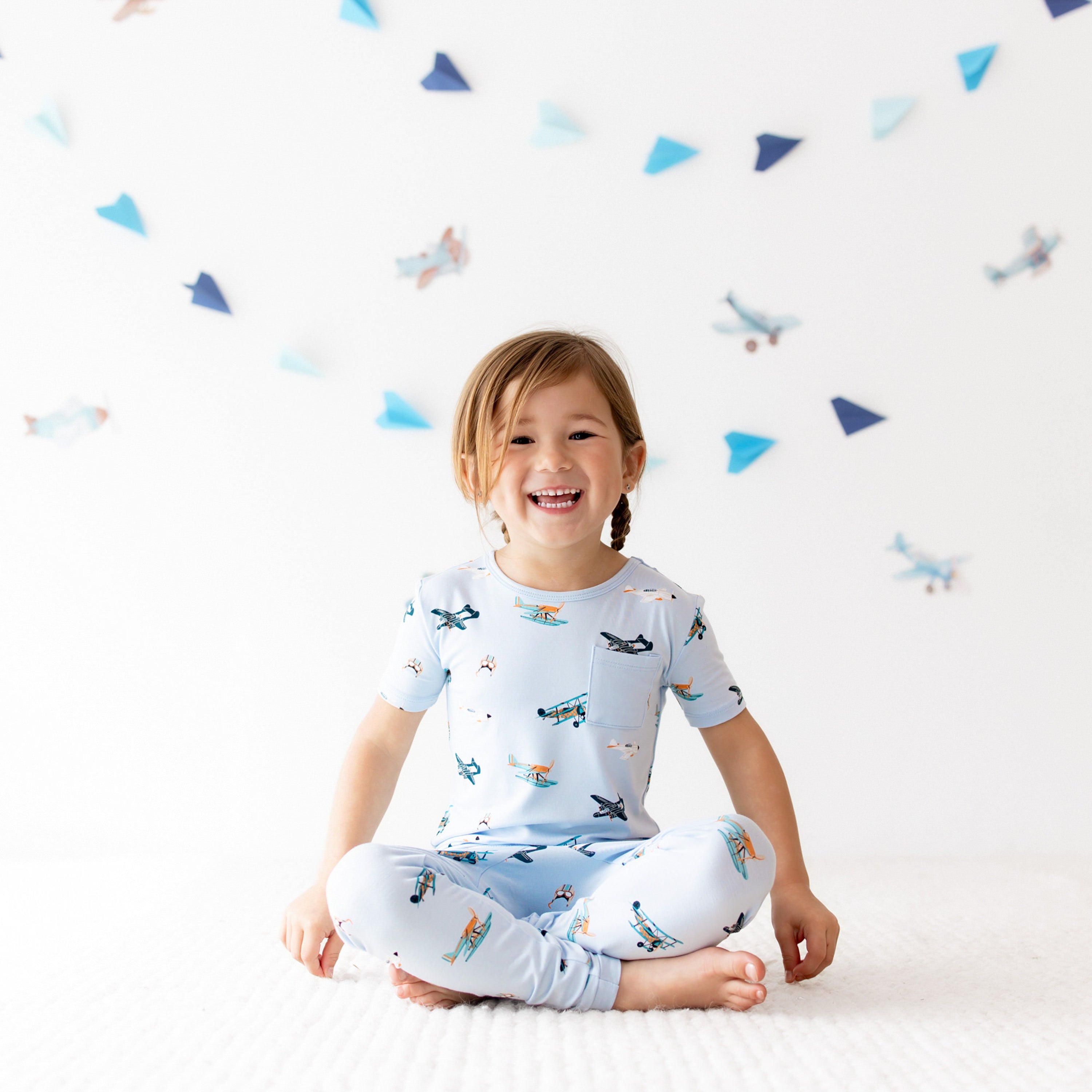 Smiling girl sitting cross legged on the floor wearing the Short Sleeve with Pants Pajamas in Take Off