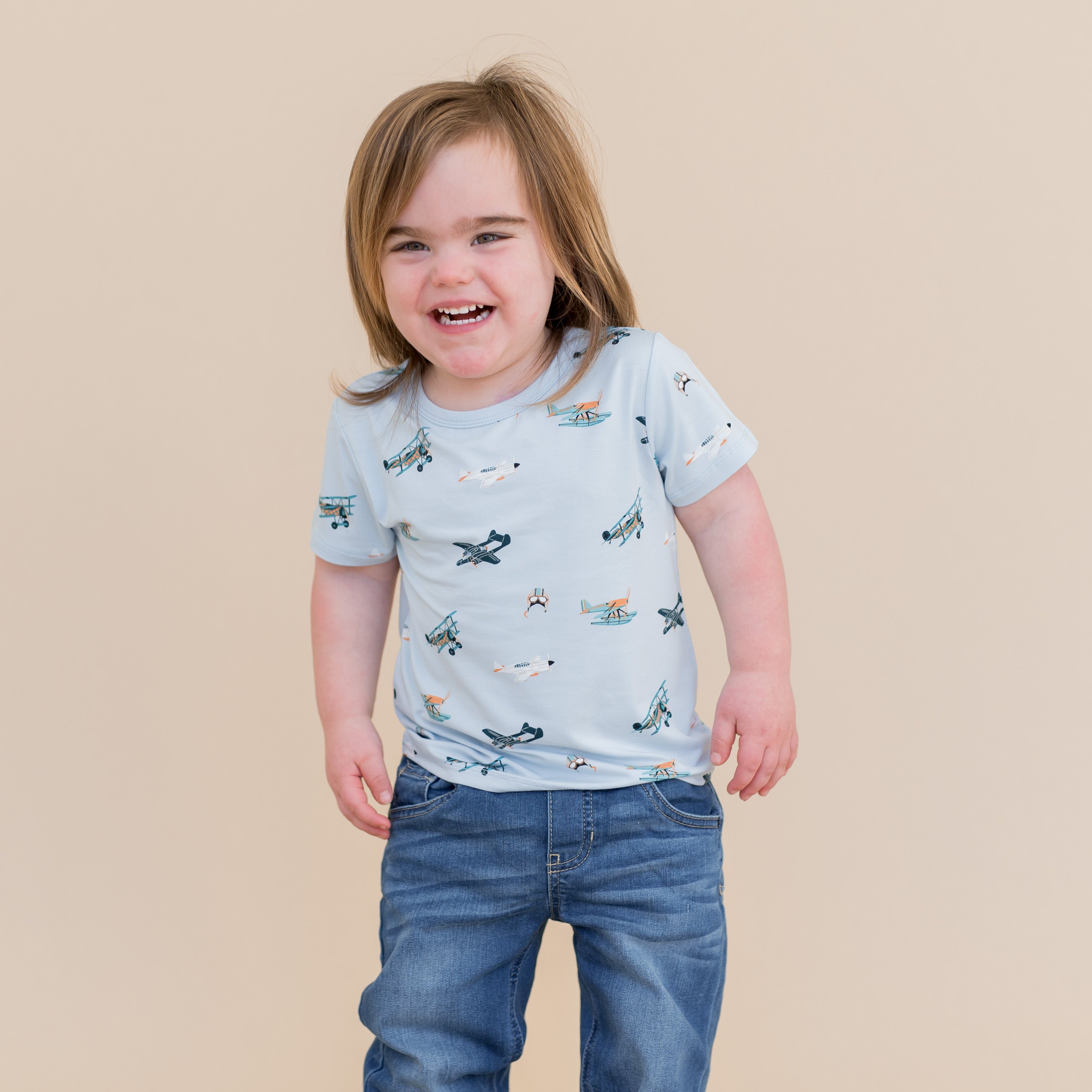 Smiling child wearing the Toddler Basic Tee in Take Off with medium wash jeans