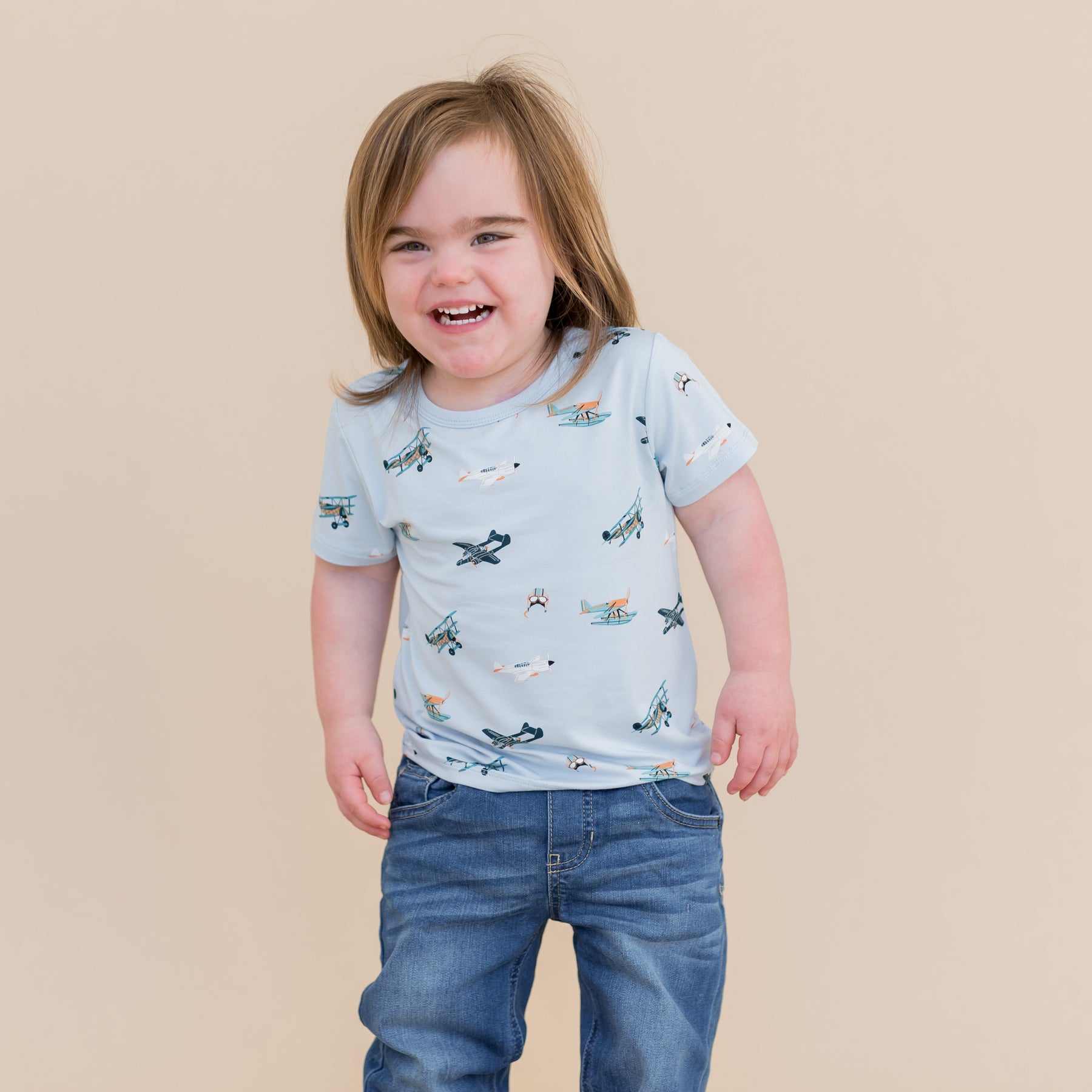Smiling child wearing the Toddler Basic Tee in Take Off with medium wash jeans
