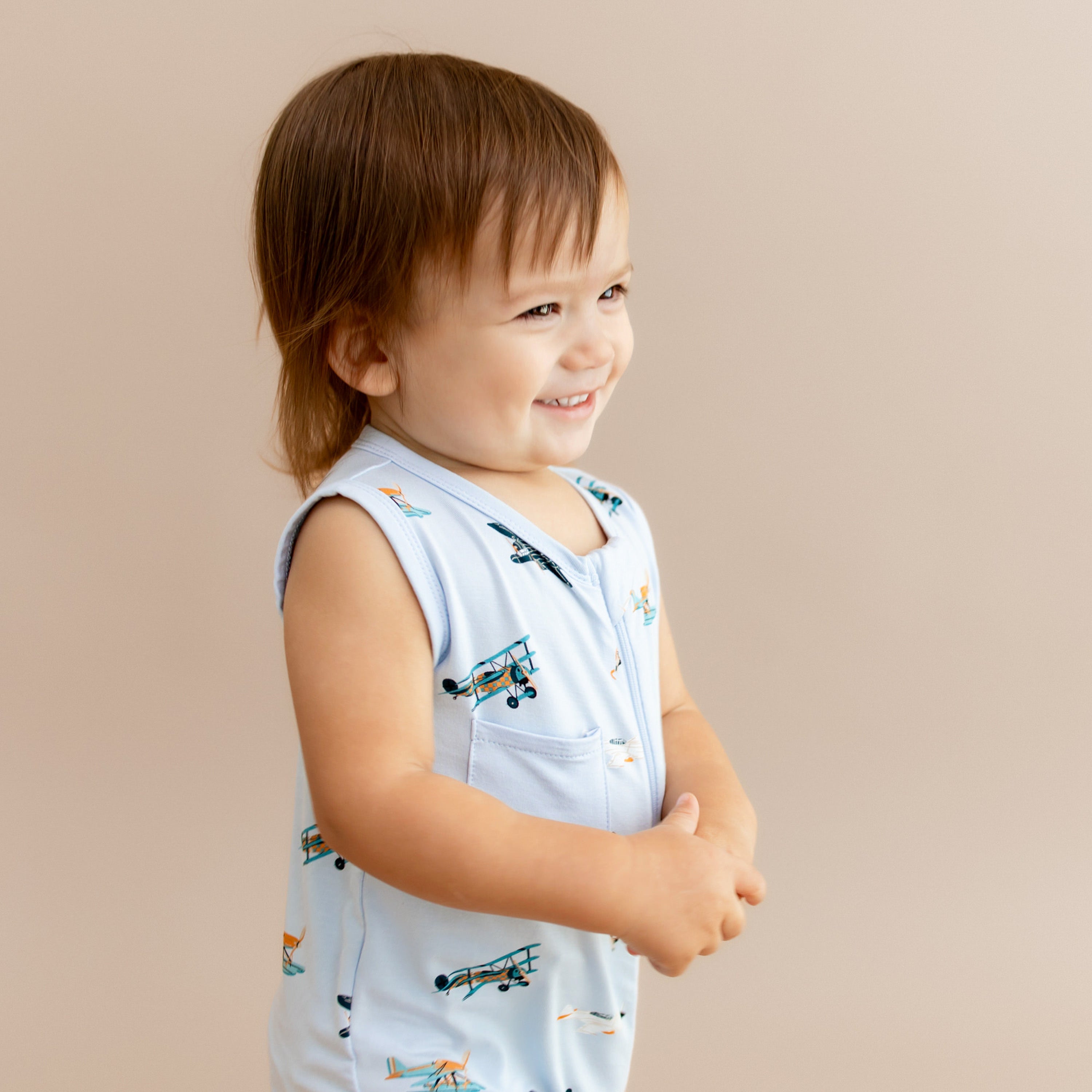 Smiling toddler looking off to the side wearing the Zippered Sleeveless Romper in Take Off