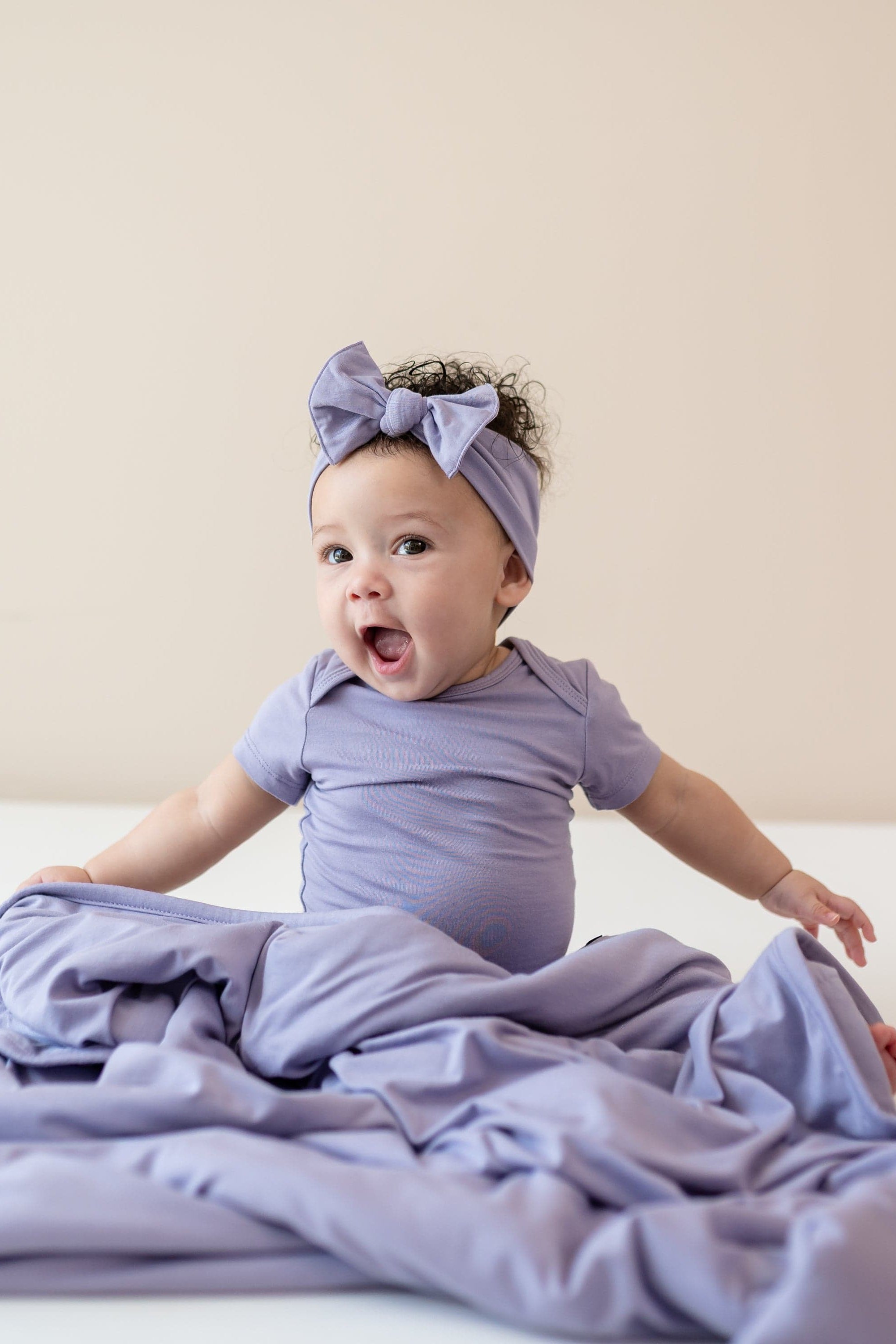 Baby sitting with Baby Blanket in Taro 1.0 wearing matching bodysuit and bow