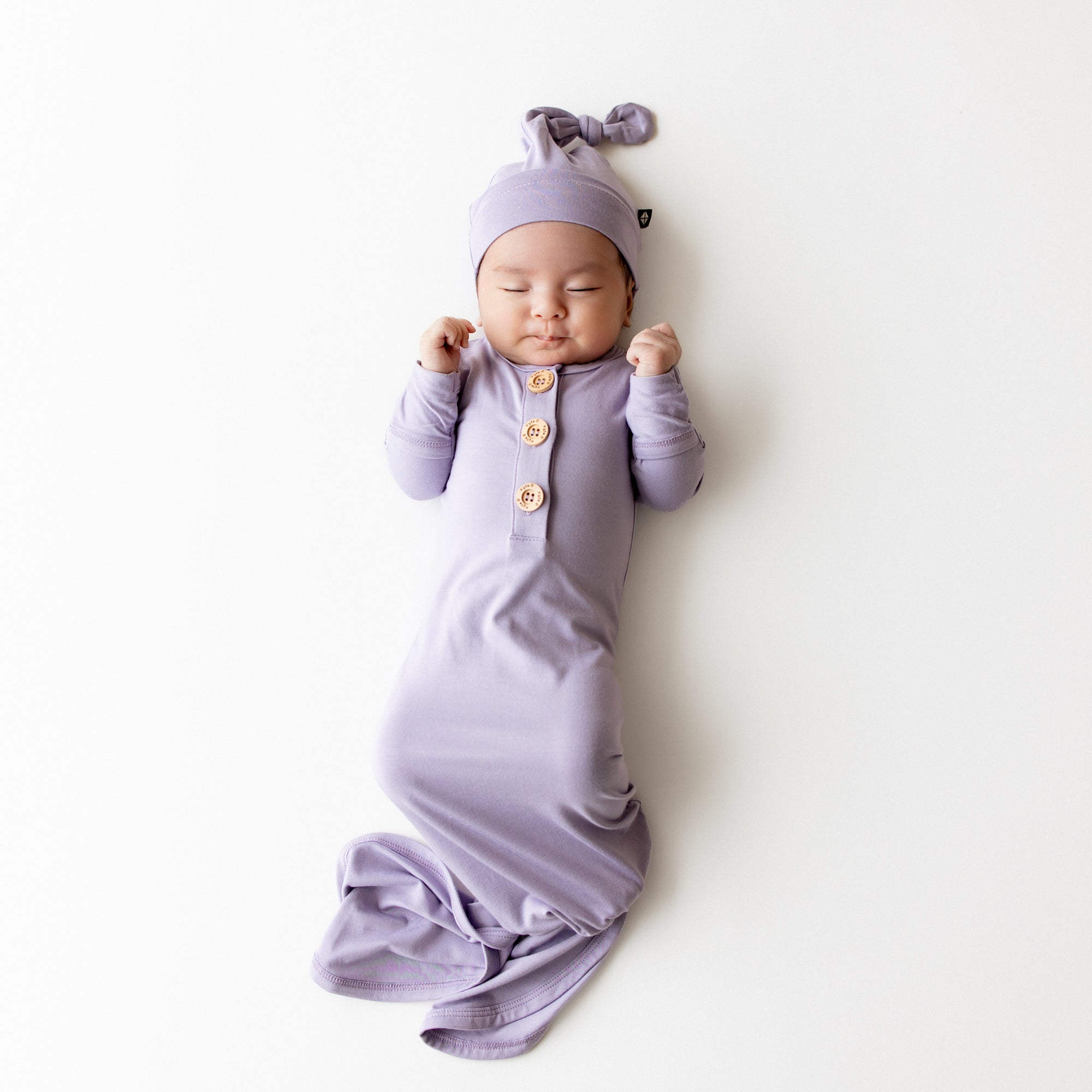 Baby sleeping in a kyte baby knotted gown in a purple color with wooden buttons and matching cap