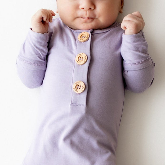 Baby sleeping in a kyte baby knotted gown in a purple color with wooden buttons and matching cap