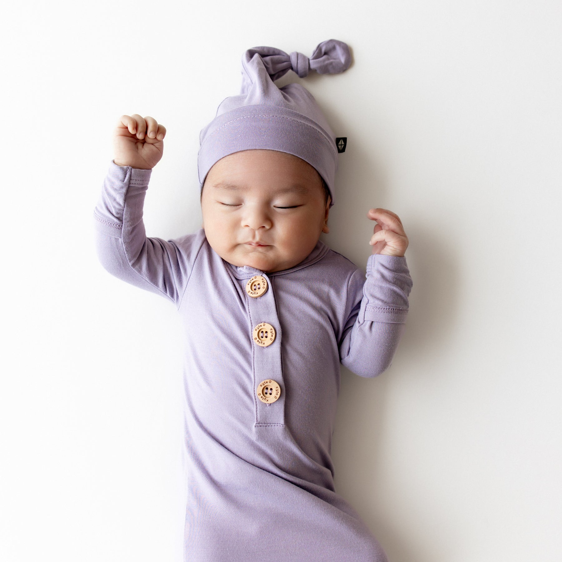 Baby in a purple outfit with buttons and a matching hat on a white background