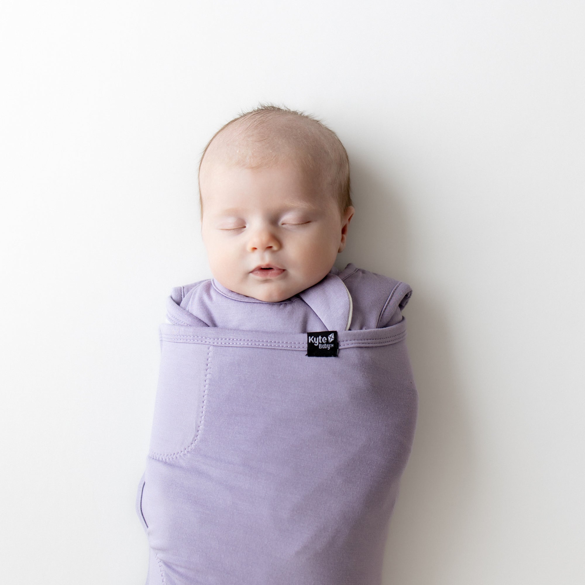 Baby swaddled in a purple swaddler on a white background