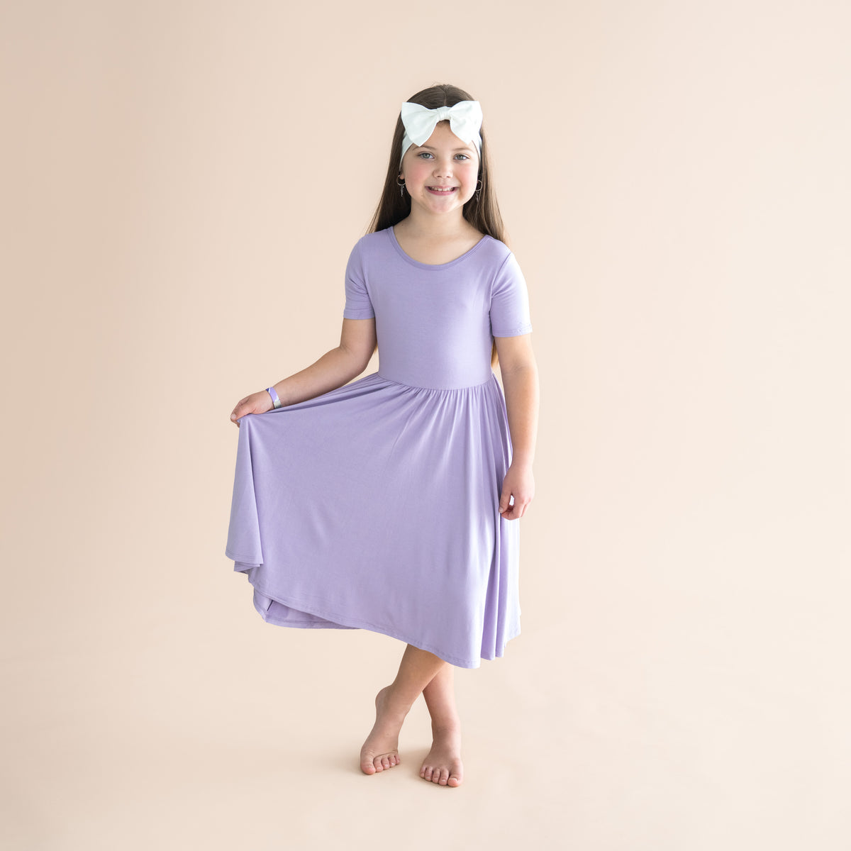 Young girl wearing a light purple dress and headband on a beige background