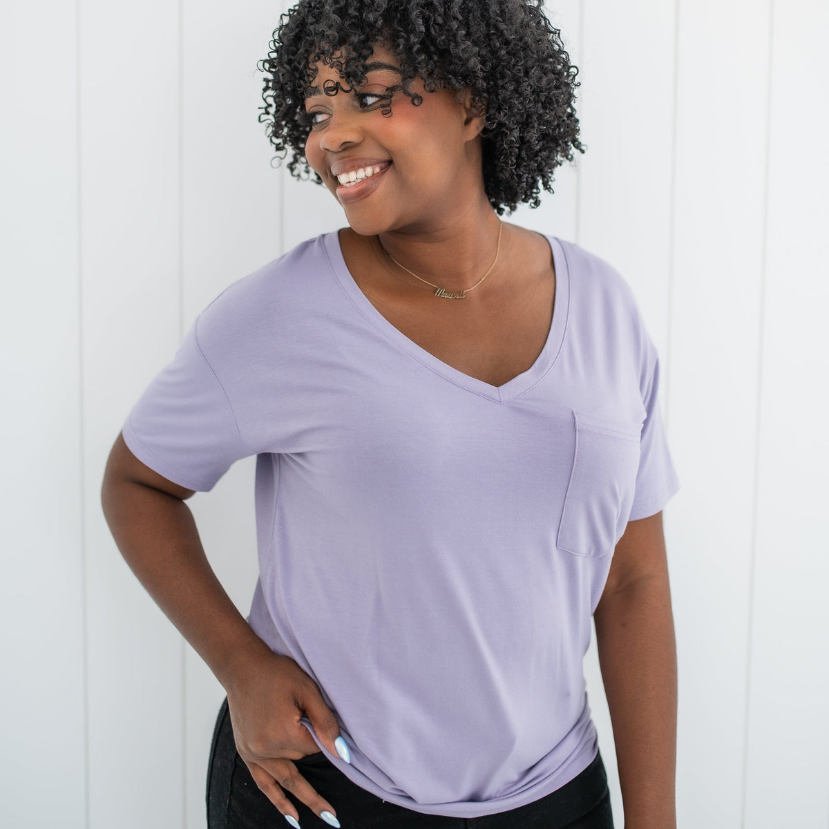 Smiling female wearing the Women’s Relaxed Fit V-Neck in Taro standing in front of a white paneled wall