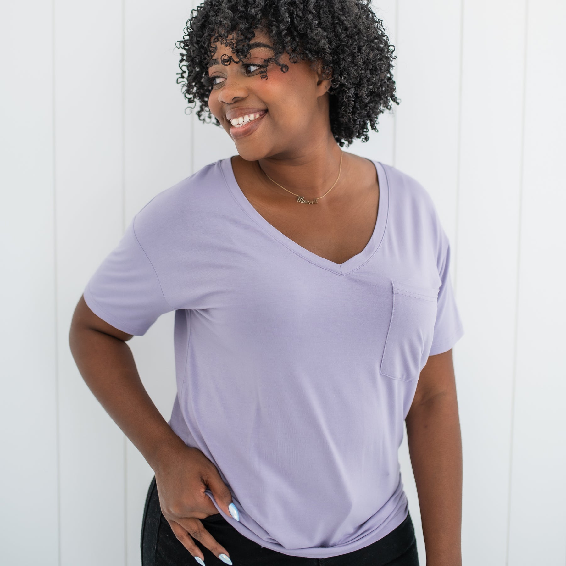 Smiling female wearing the Women’s Relaxed Fit V-Neck in Taro standing in front of a white paneled wall