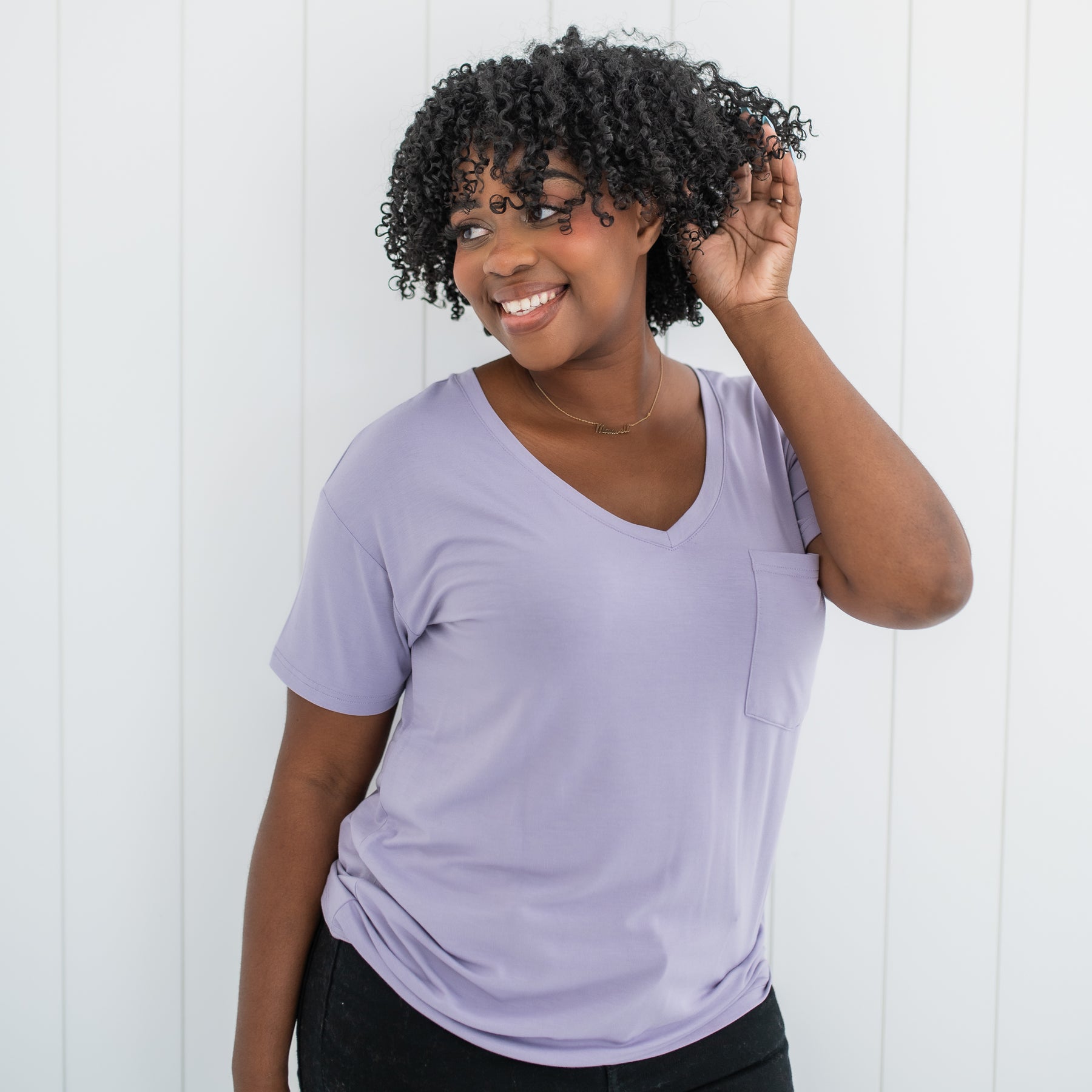 Smiling female model looking off to the side with one hand in her hair wearing the Women’s Relaxed Fit V-Neck in Taro