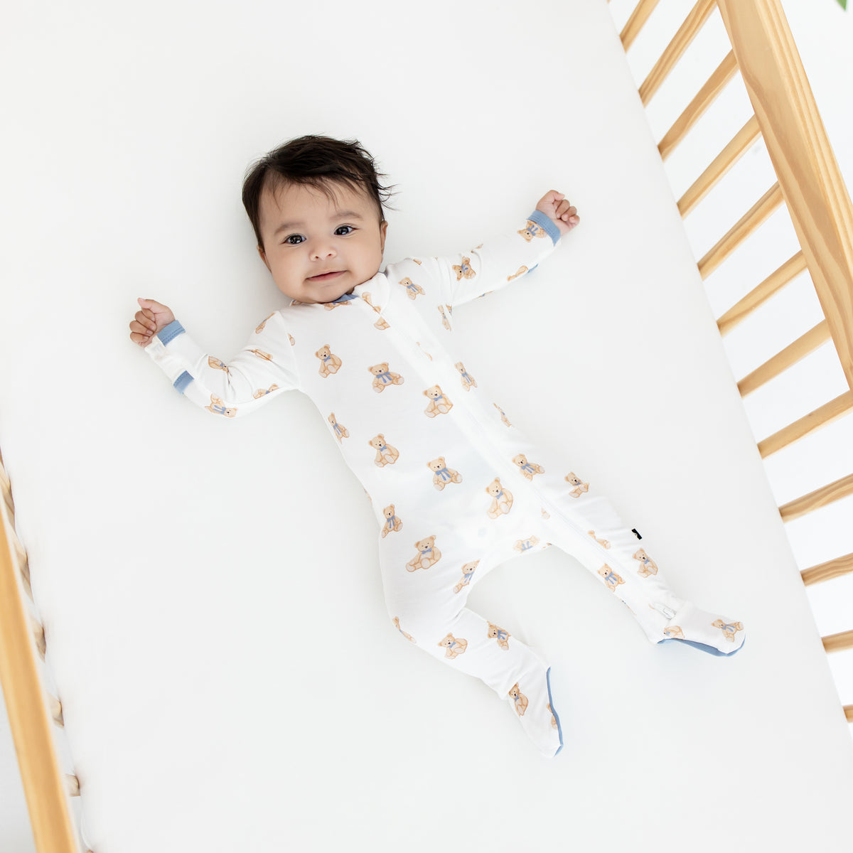Baby in teddy bear zippered footie laying in a crib