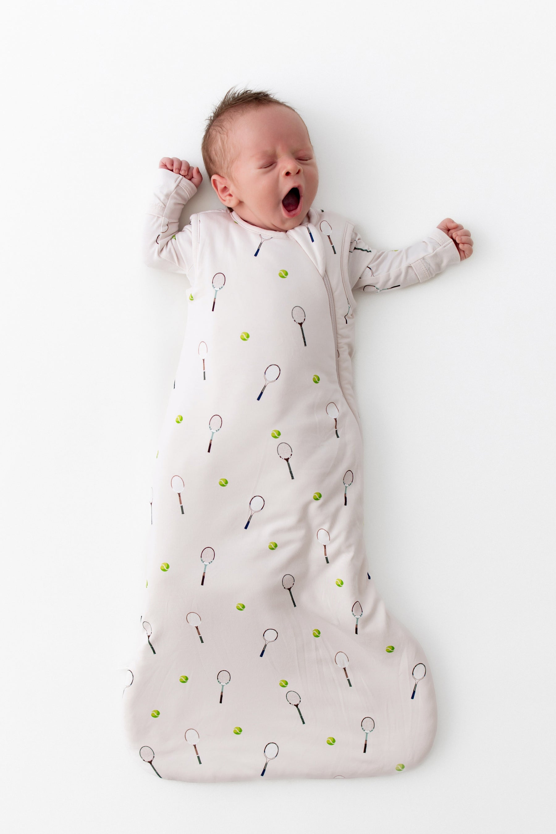 Baby sleeping in a tennis patterned sleep bag on a white background