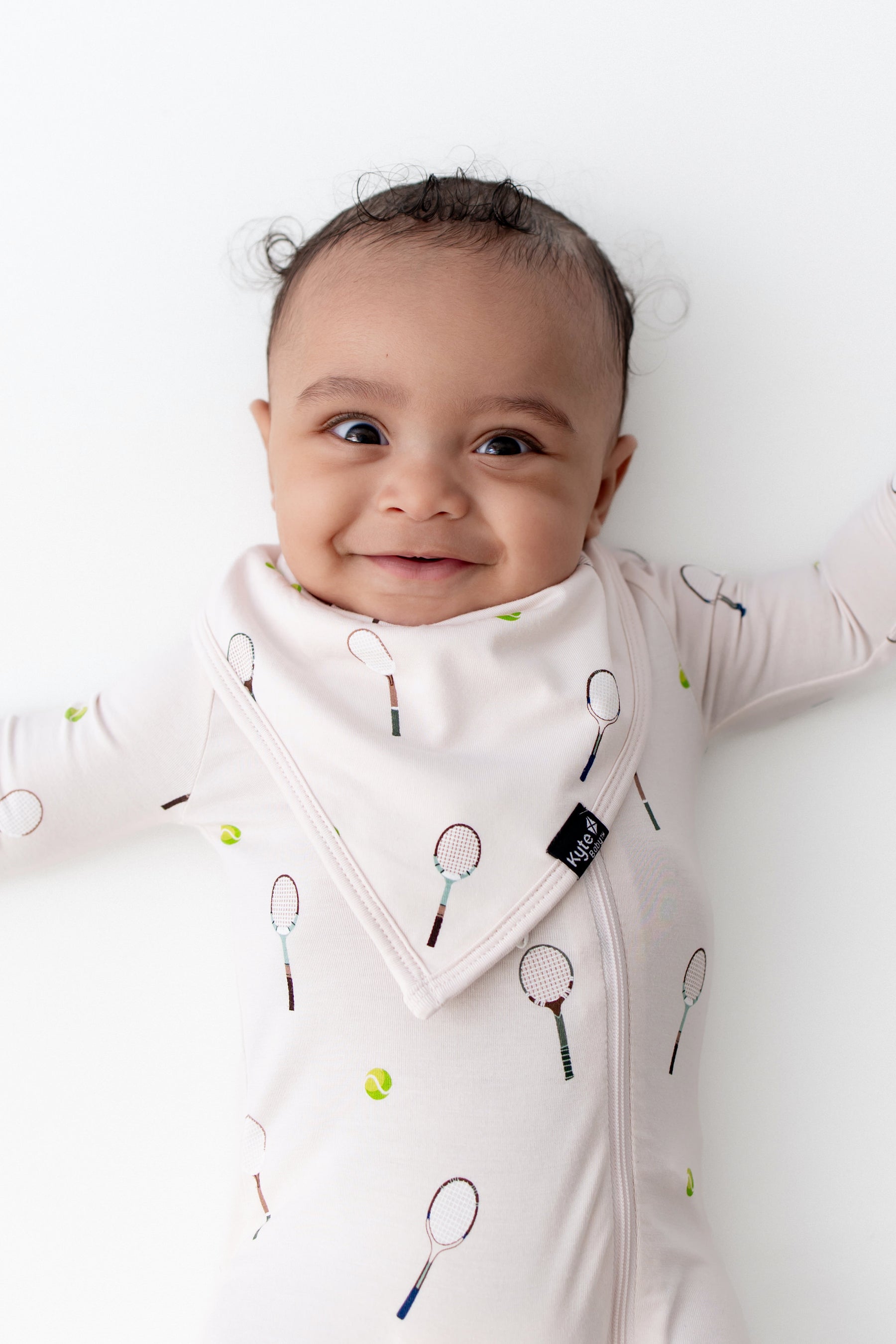 Baby wearing a white onesie with tennis racket print on a white background