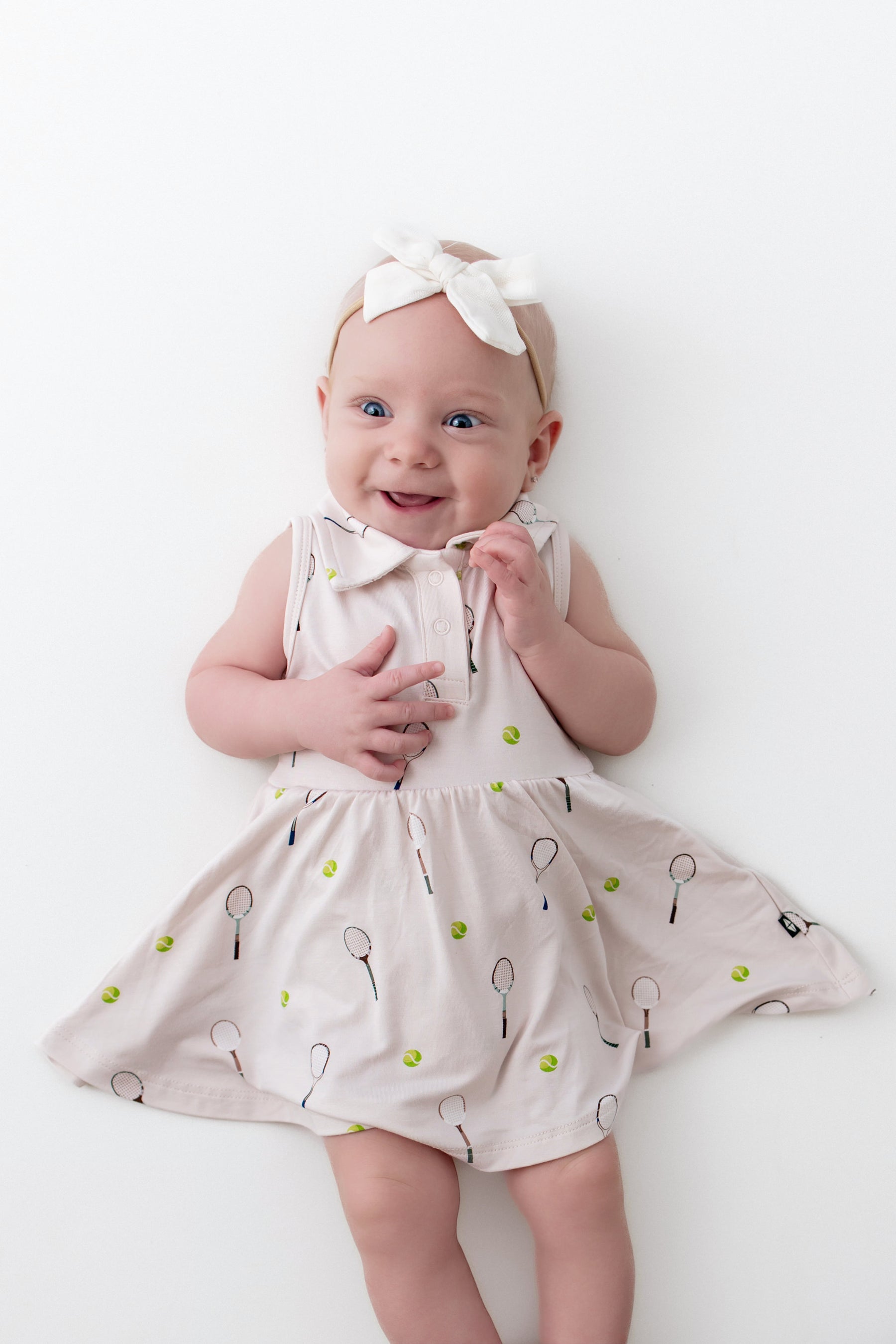 Baby wearing a dress with tennis racket pattern on a white background