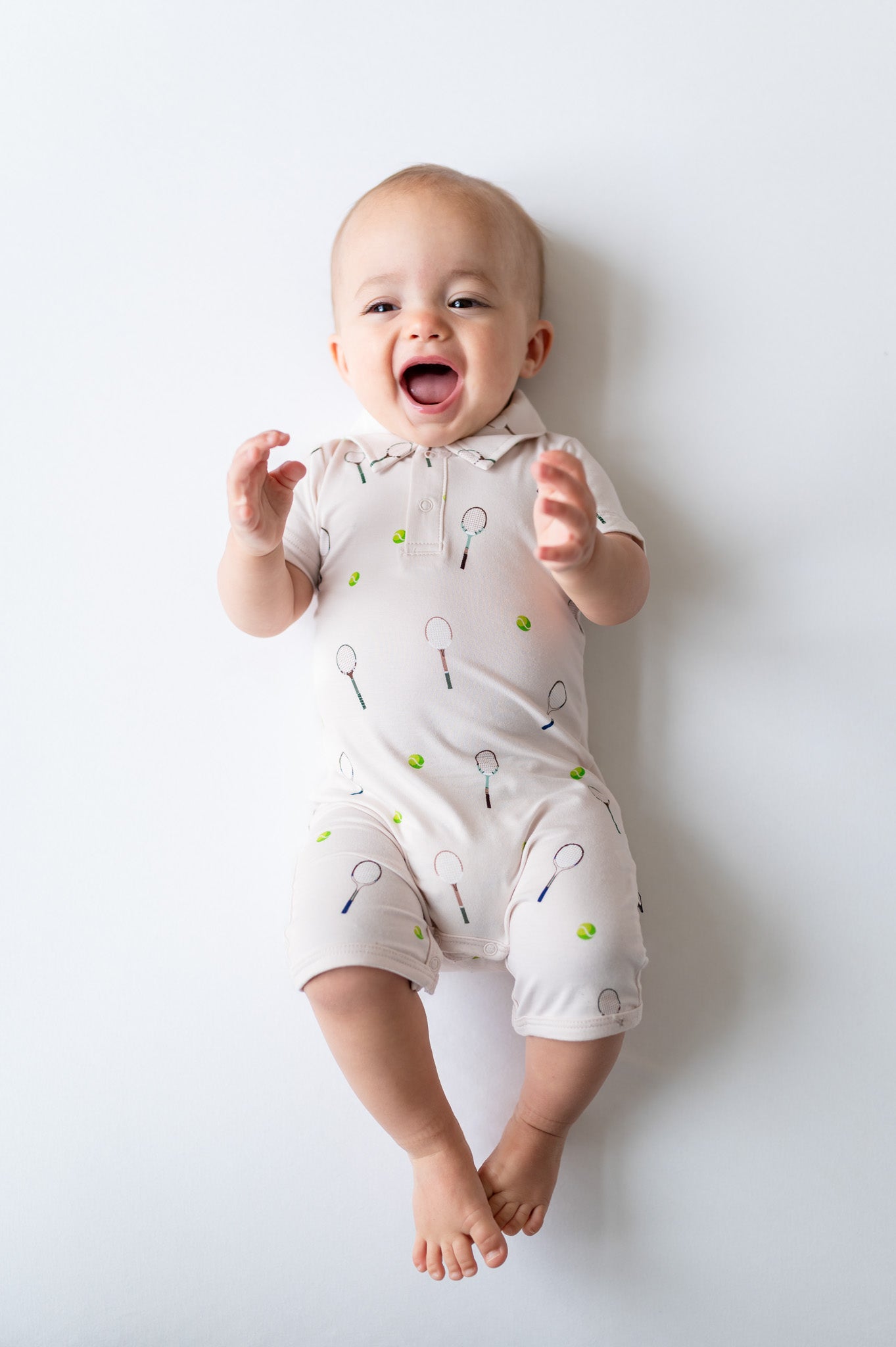 Baby wearing a light-colored outfit with tennis patterns on a white background