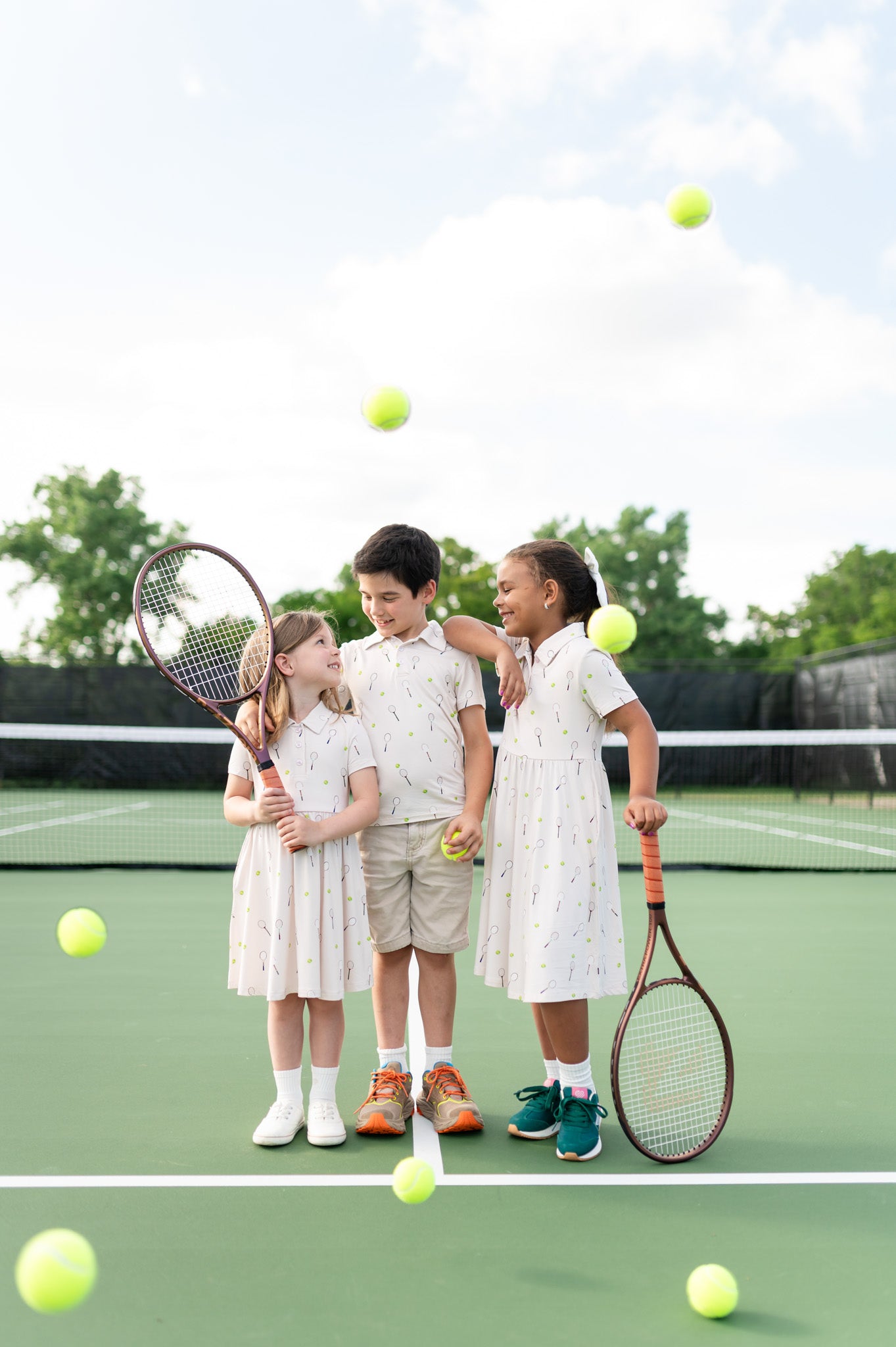 3 children wearing tennis themed outfits on a tennis court