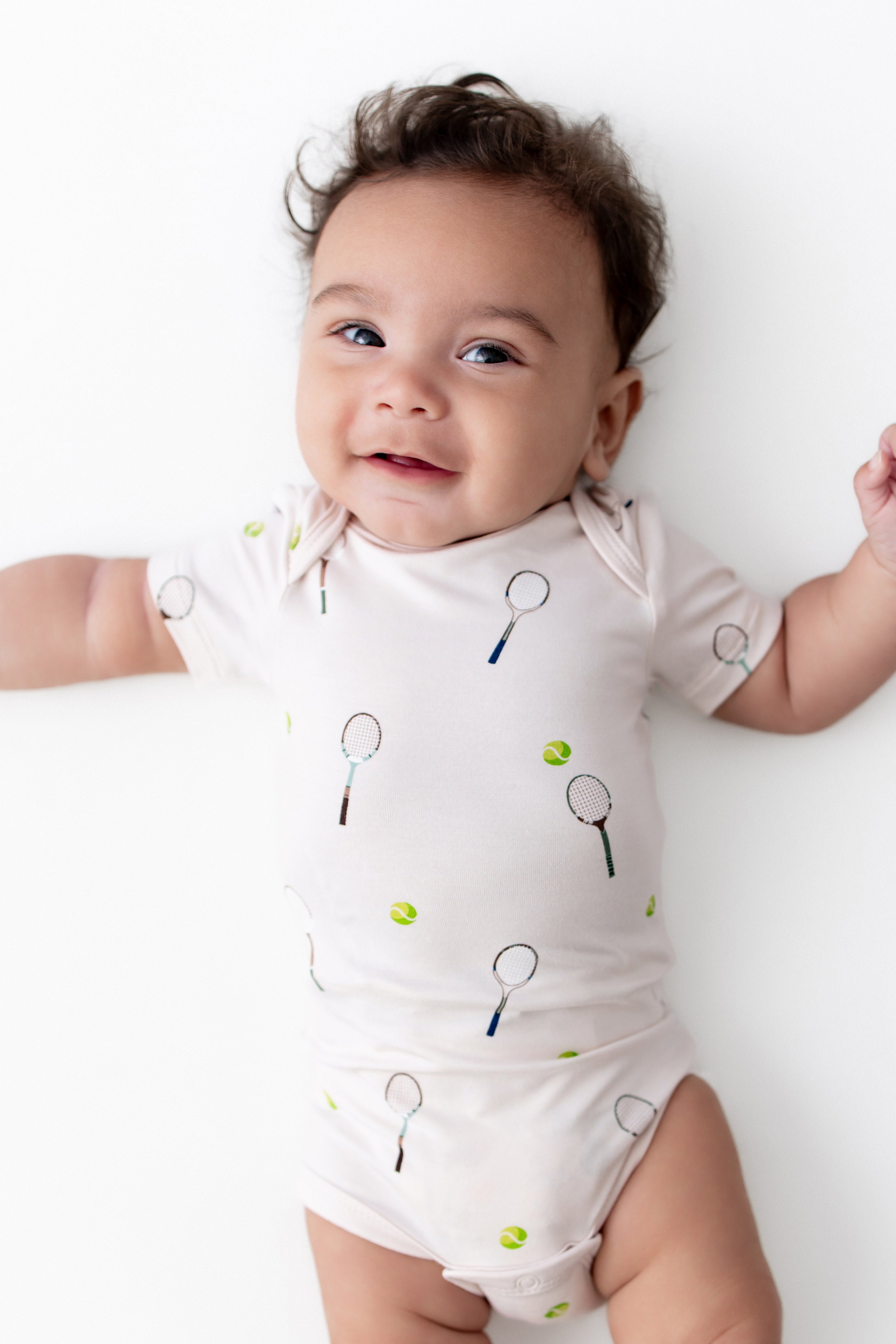 Baby wearing a onesie with tennis racket and ball prints on a white background