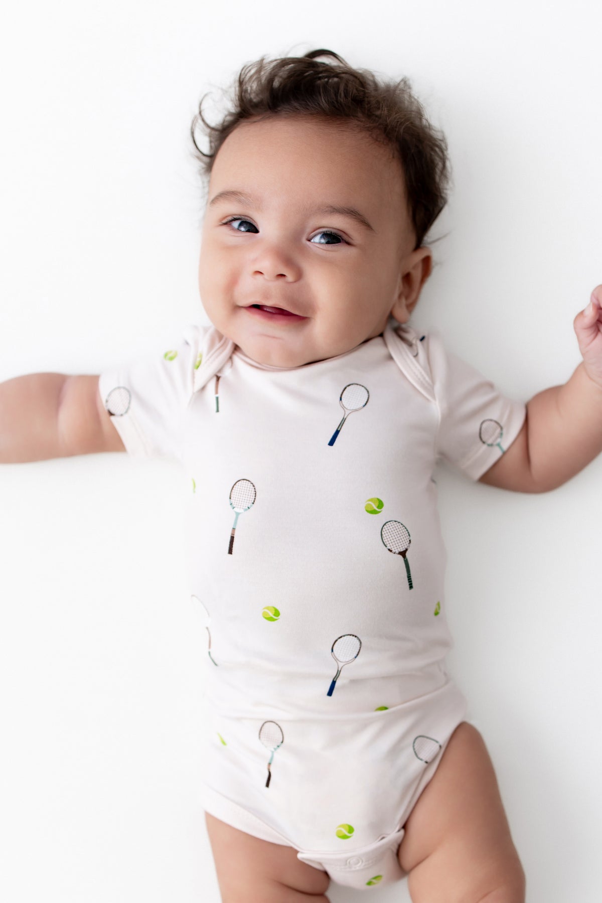 Baby wearing a onesie with tennis racket and ball prints on a white background