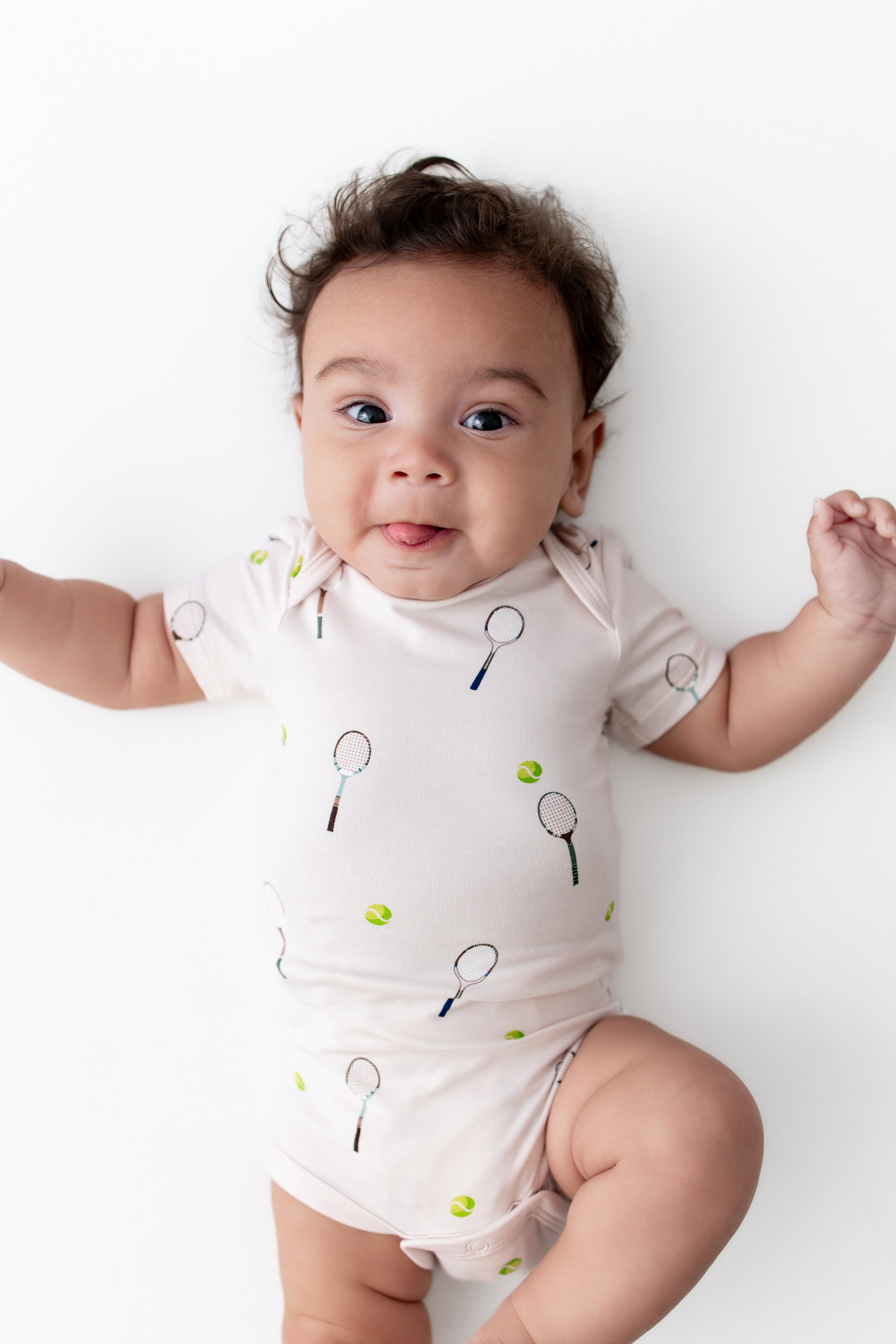 Baby wearing a onesie with tennis racket and ball pattern on a white background