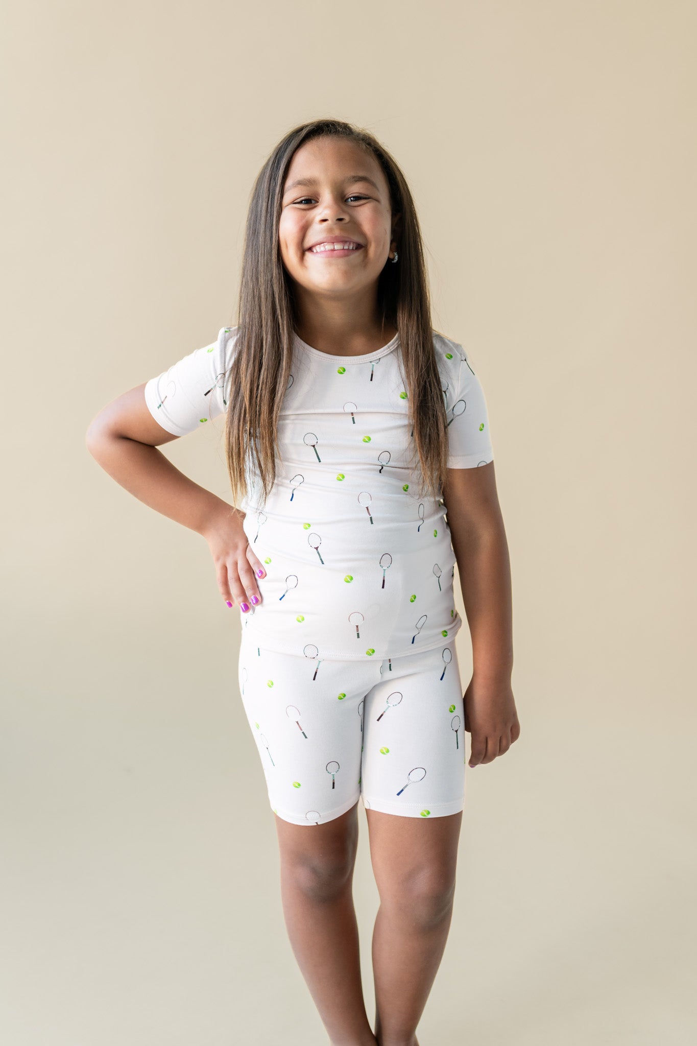 Young girl wearing a white outfit with patterned design against a beige background