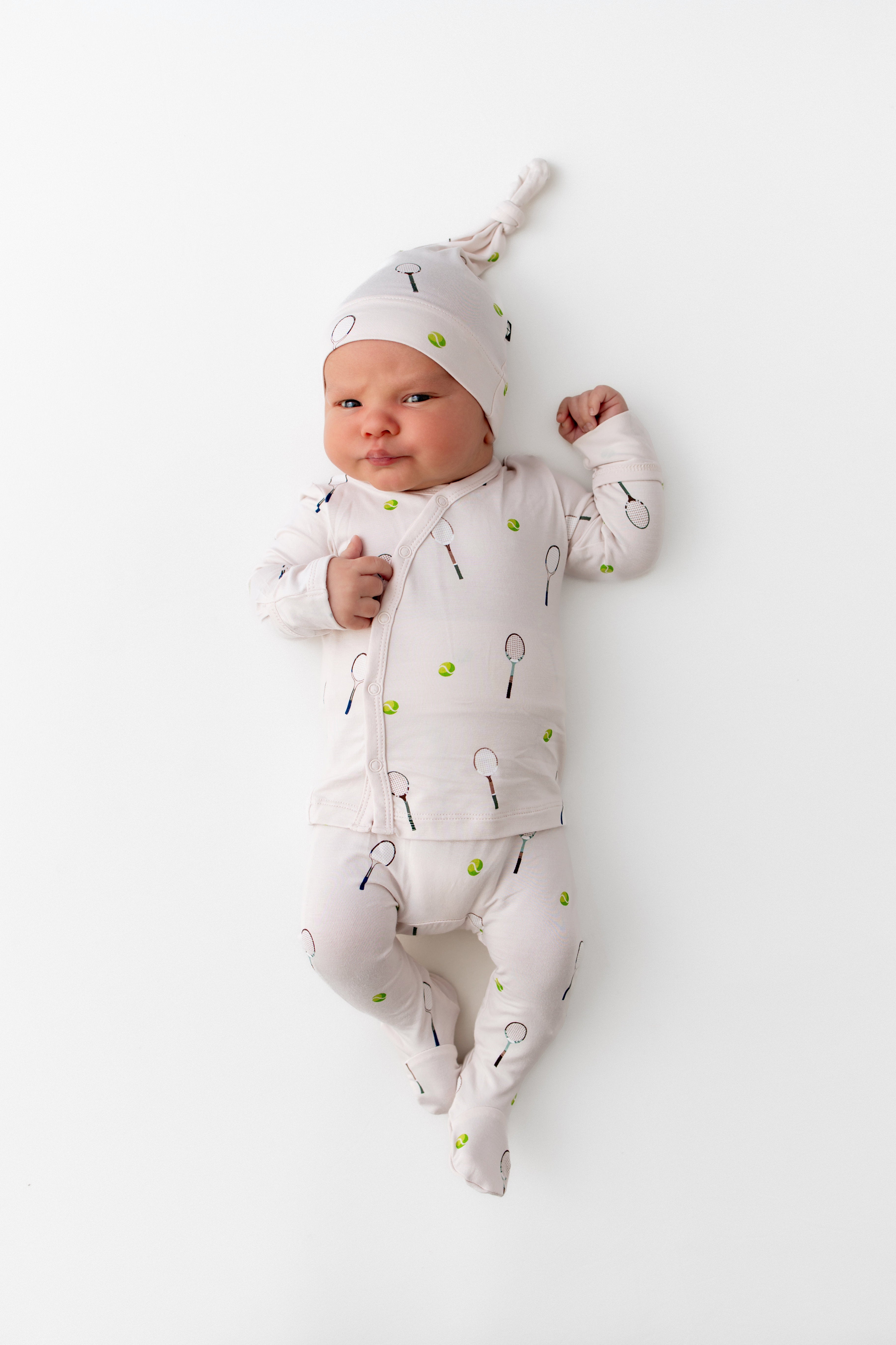 Baby in a white outfit with green tennis balls and black tennis rackets on a white background
