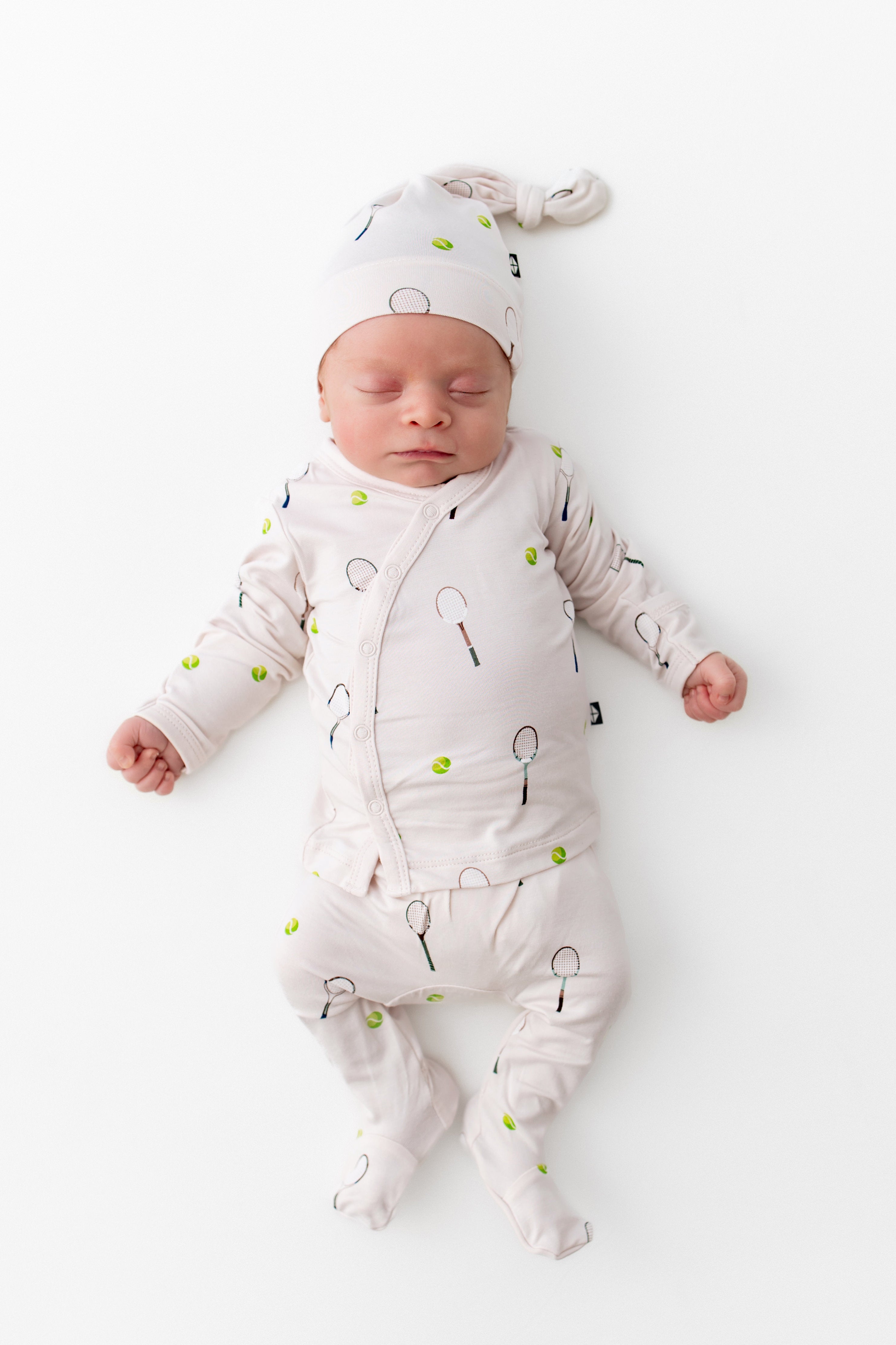 Newborn baby wearing a white outfit with tennis patterns on a white background