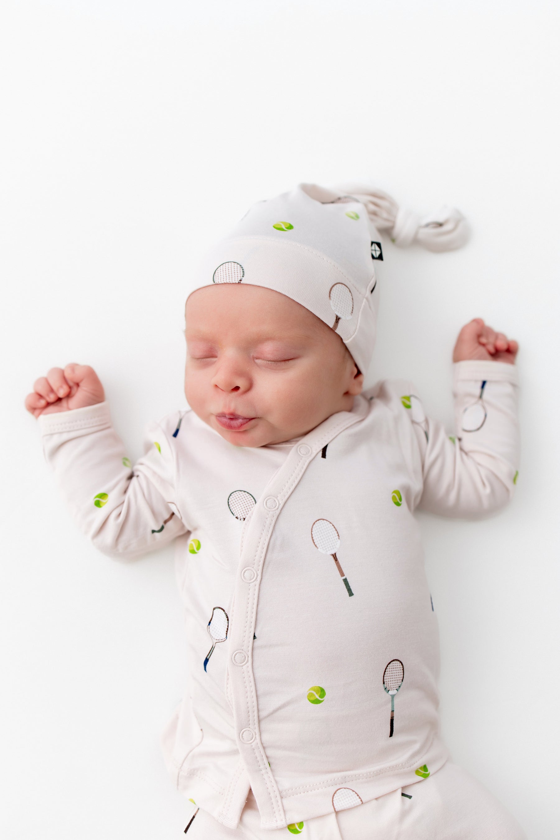 Newborn baby wearing a white outfit with tennis patterns on a white background