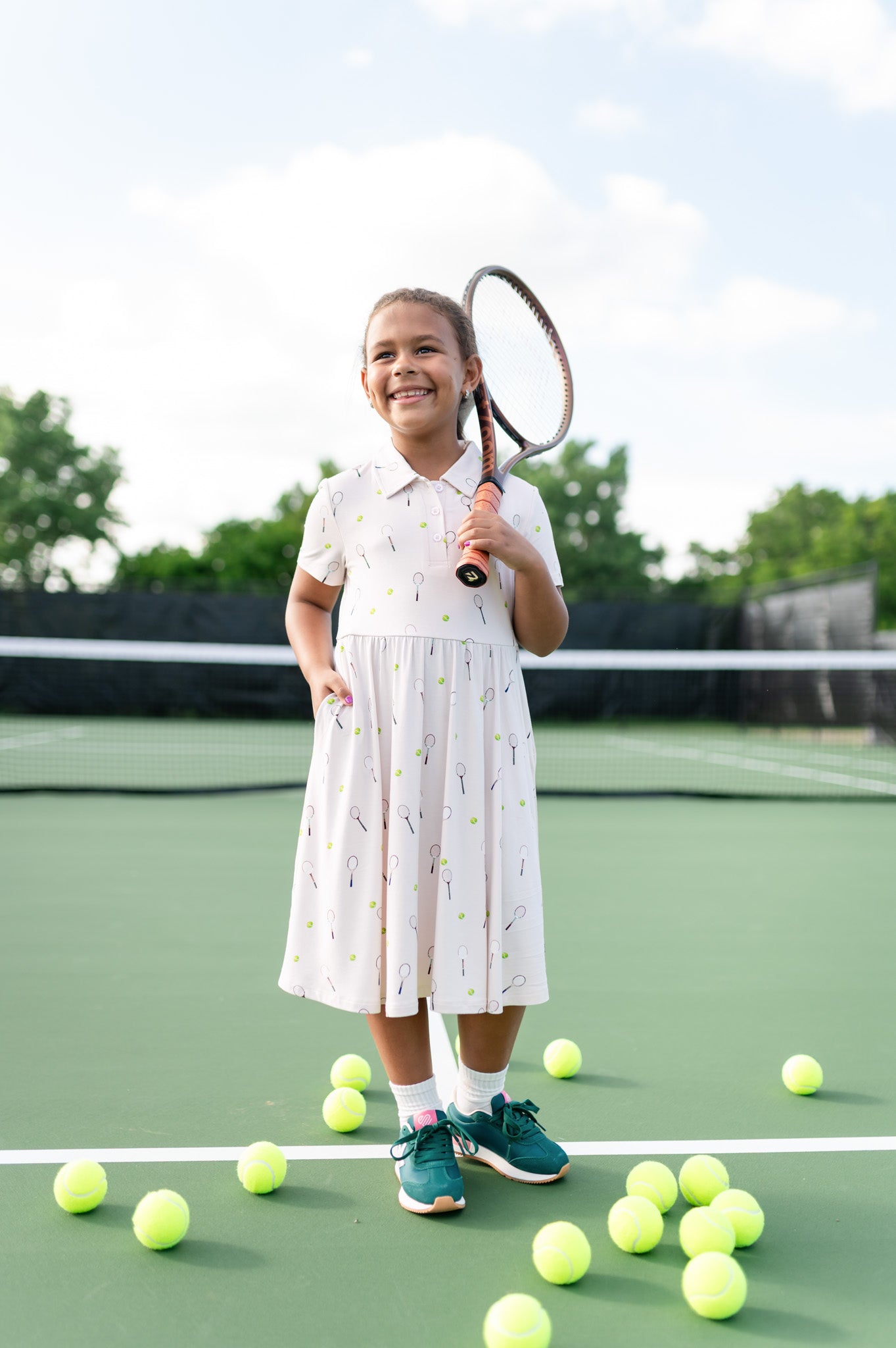 Young girl on a tennis court holding a racket with tennis balls around her