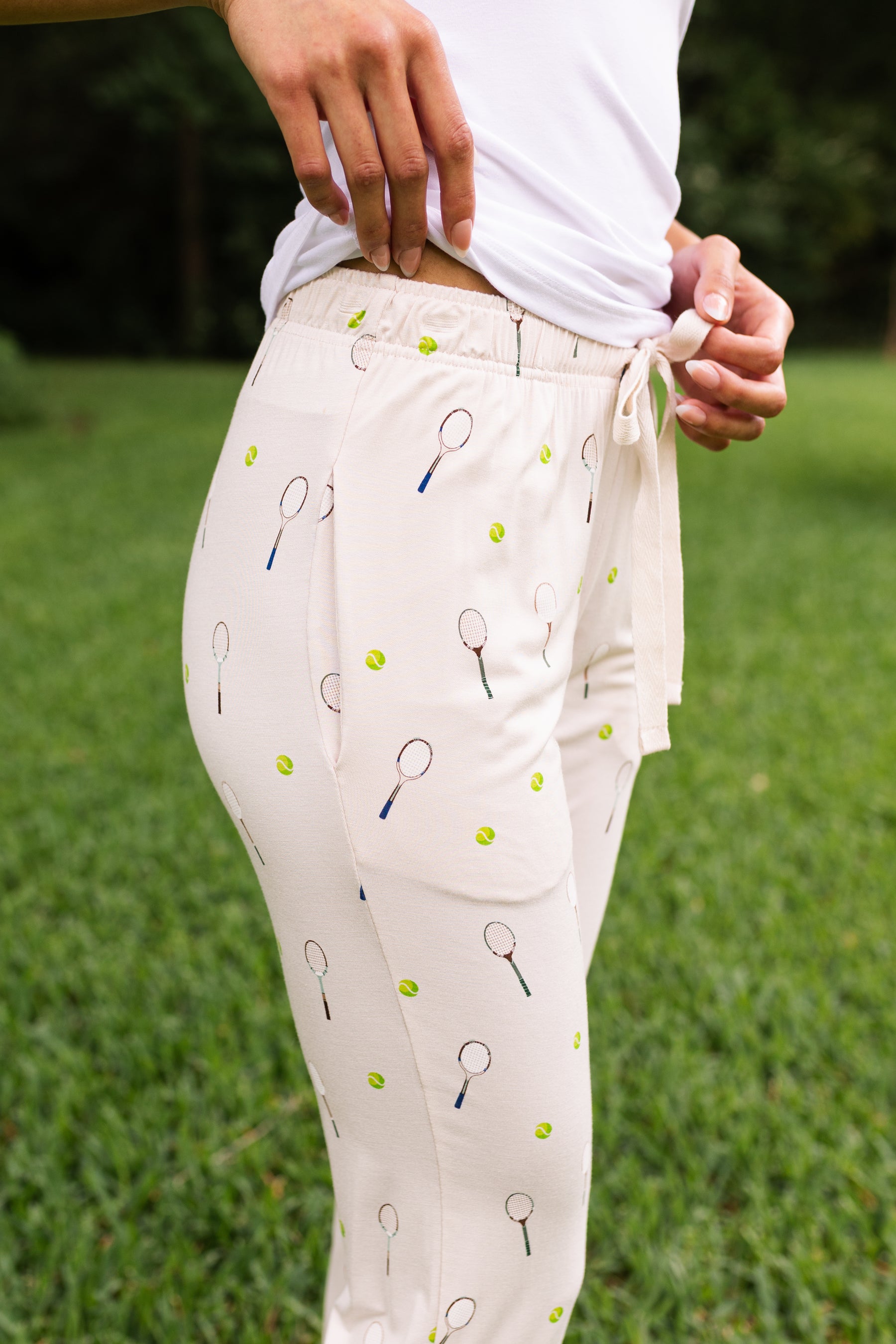 Person wearing light-colored pants with tennis racket and ball pattern on grass background
