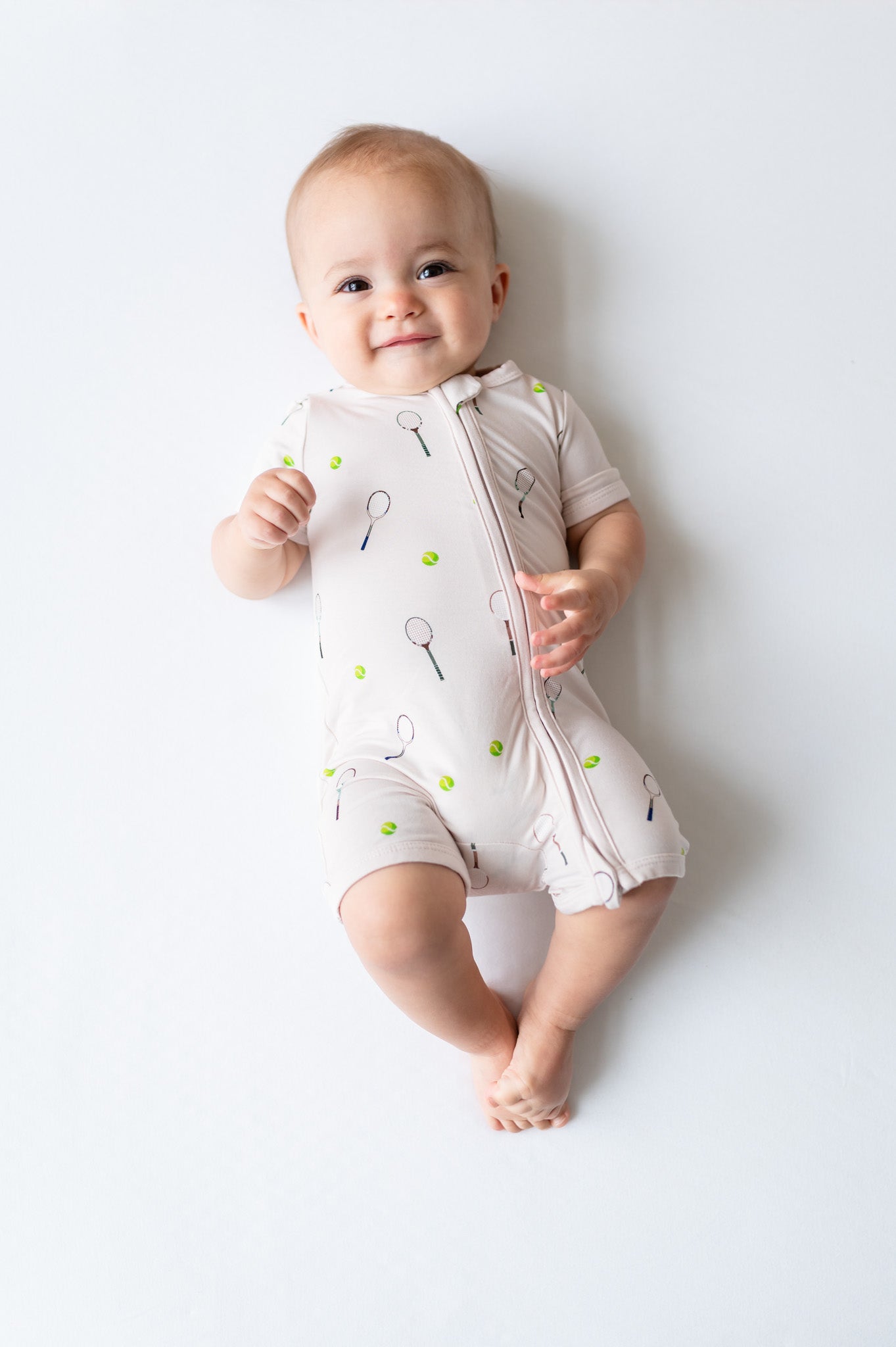 Baby wearing a white romper onesie with tennis pattern on a light gray background