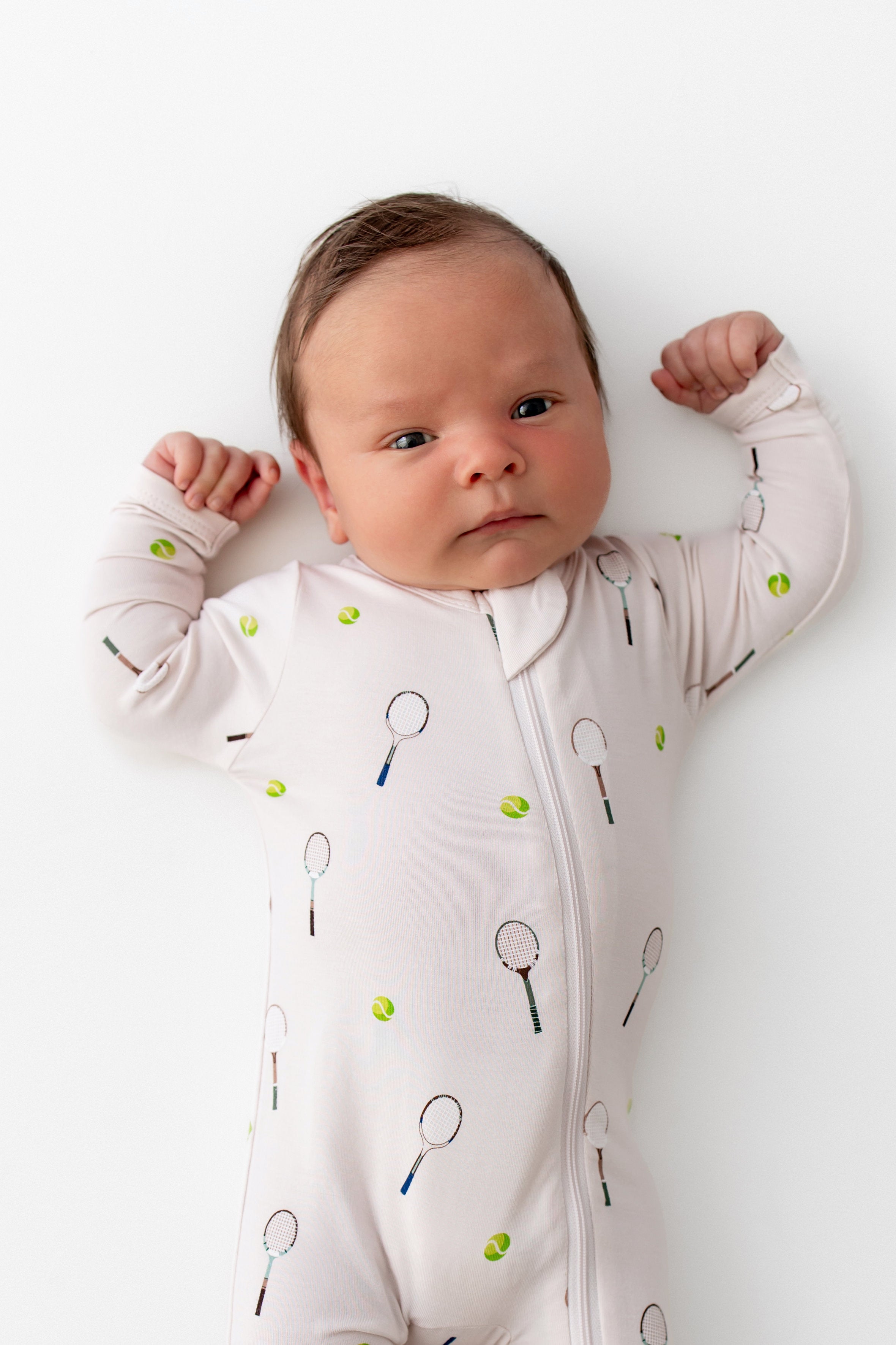 Baby wearing a onesie with tennis racket patterns on a white background