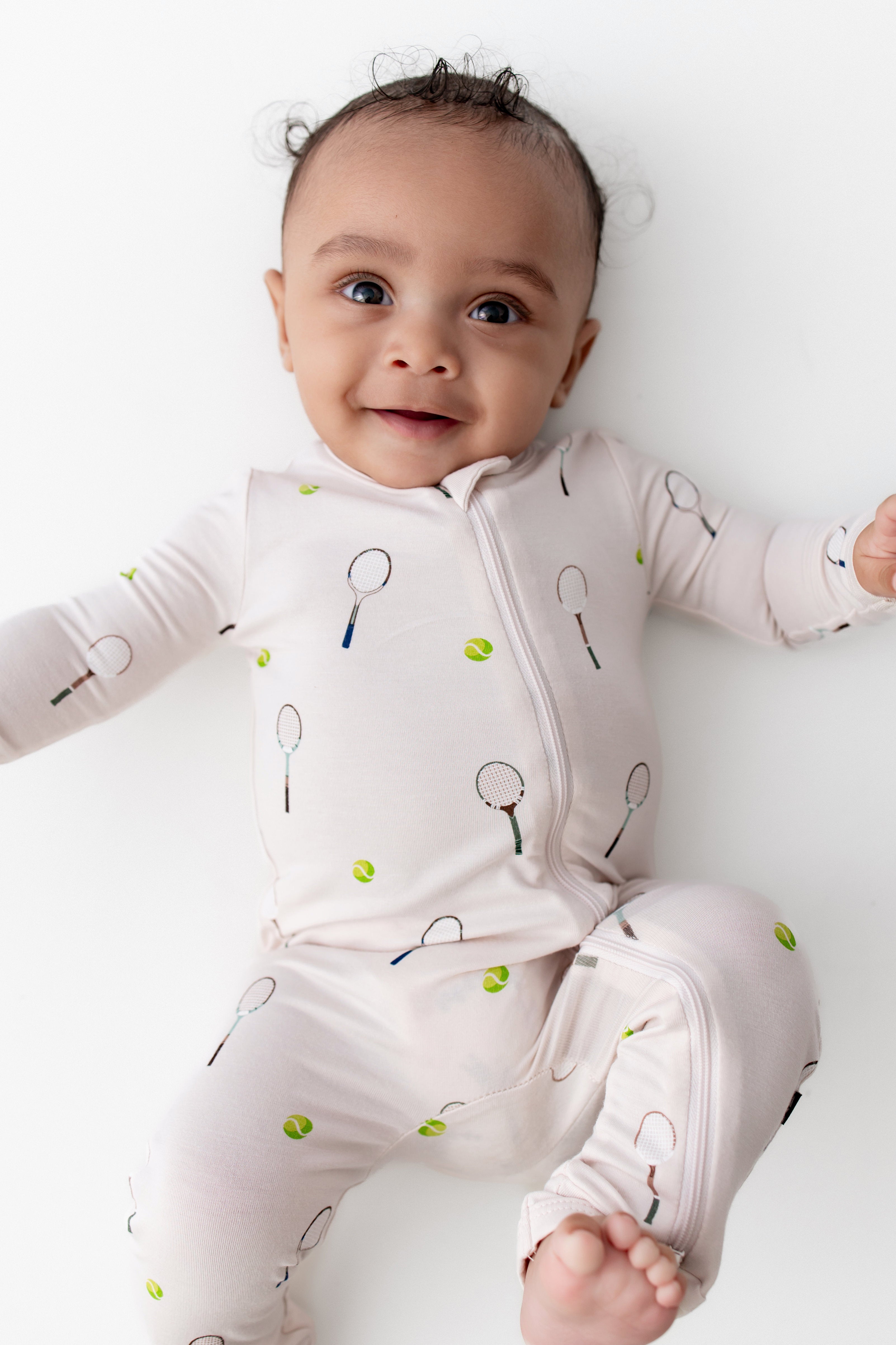 Baby wearing a onesie with tennis racket and ball pattern on a white background