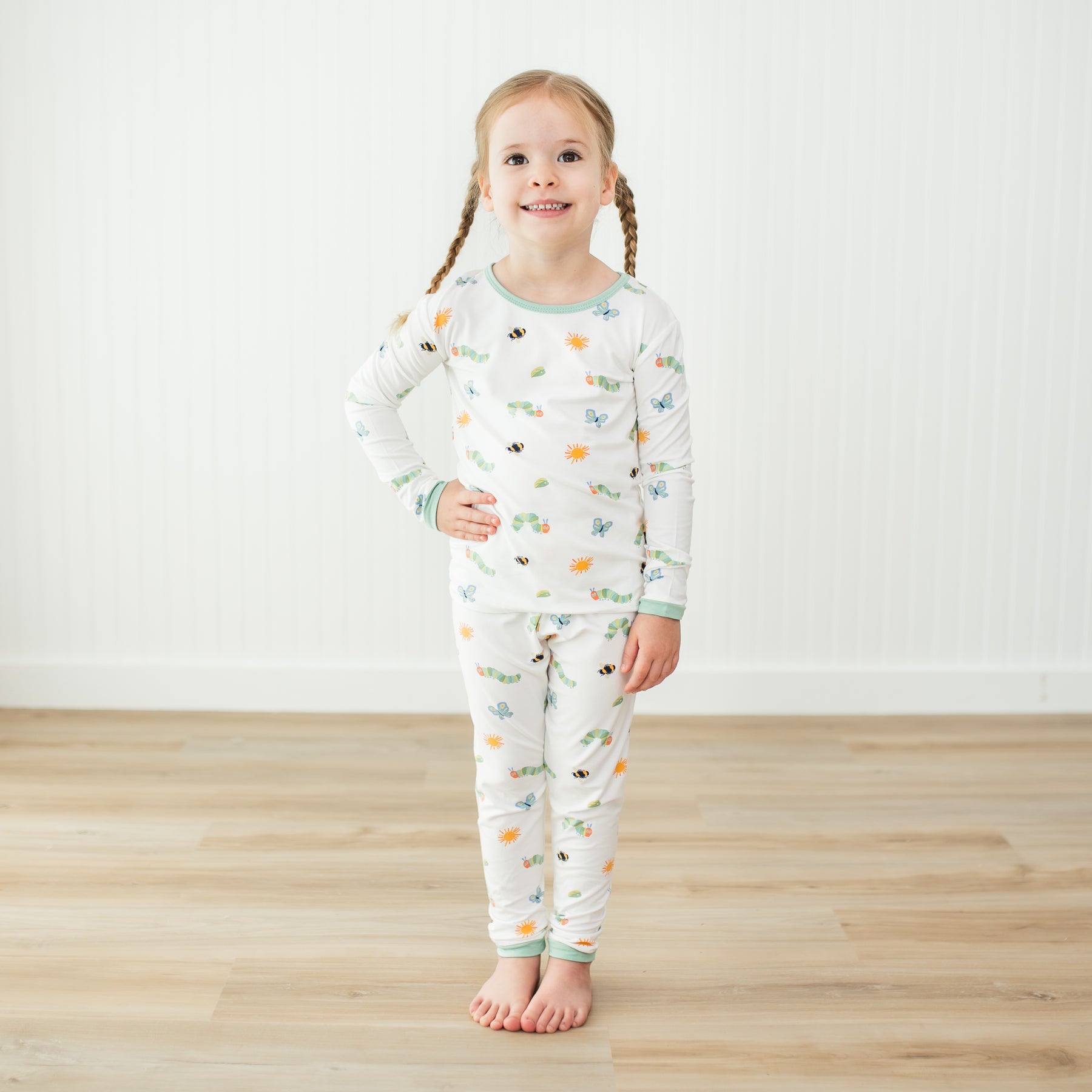 Young girl wearing an Eric Carle patterned pajama set on a wooden floor with a white wall background