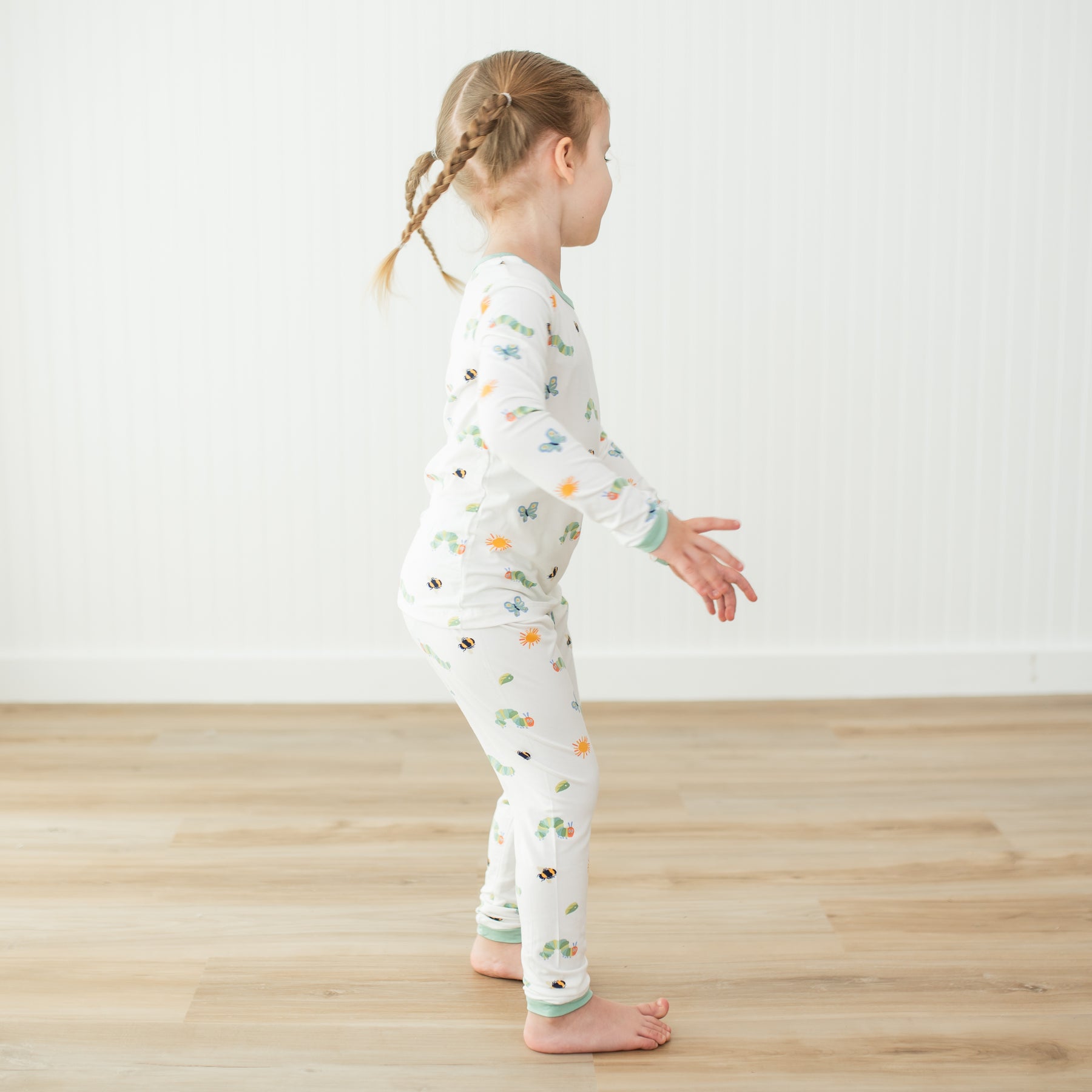 Girl spinning in a circle wearing the Long Sleeve Pajamas in The Very Hungry Caterpillar™ and Friends on a light wooden floor in front of a white paneled wall