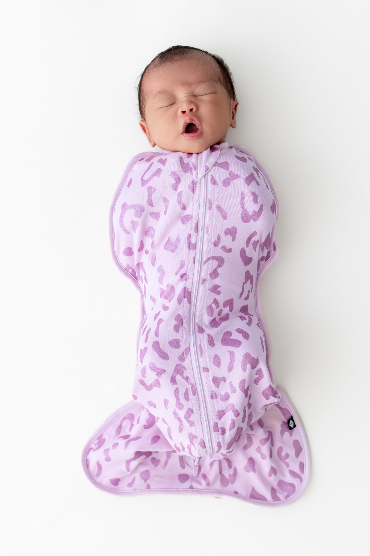 Baby yawning in a Thistle Leopard print Swaddle bag on a white background