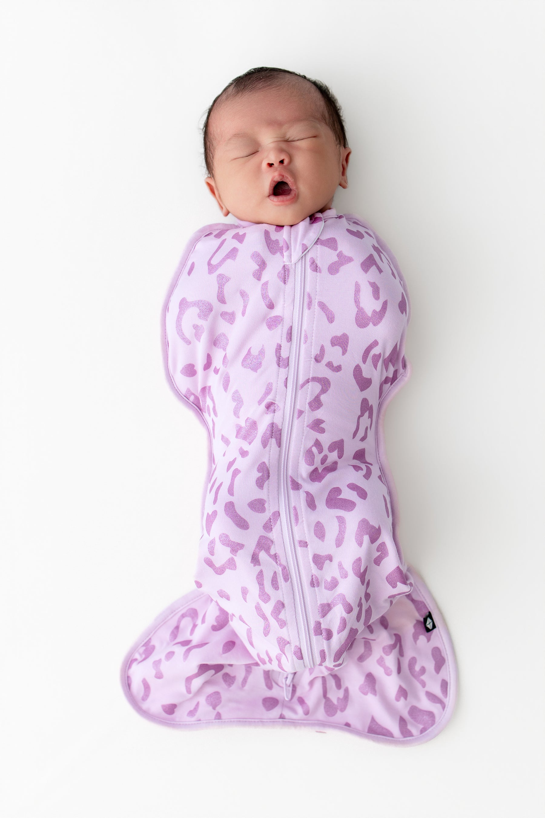 Baby yawning in a Thistle Leopard print Swaddle bag on a white background