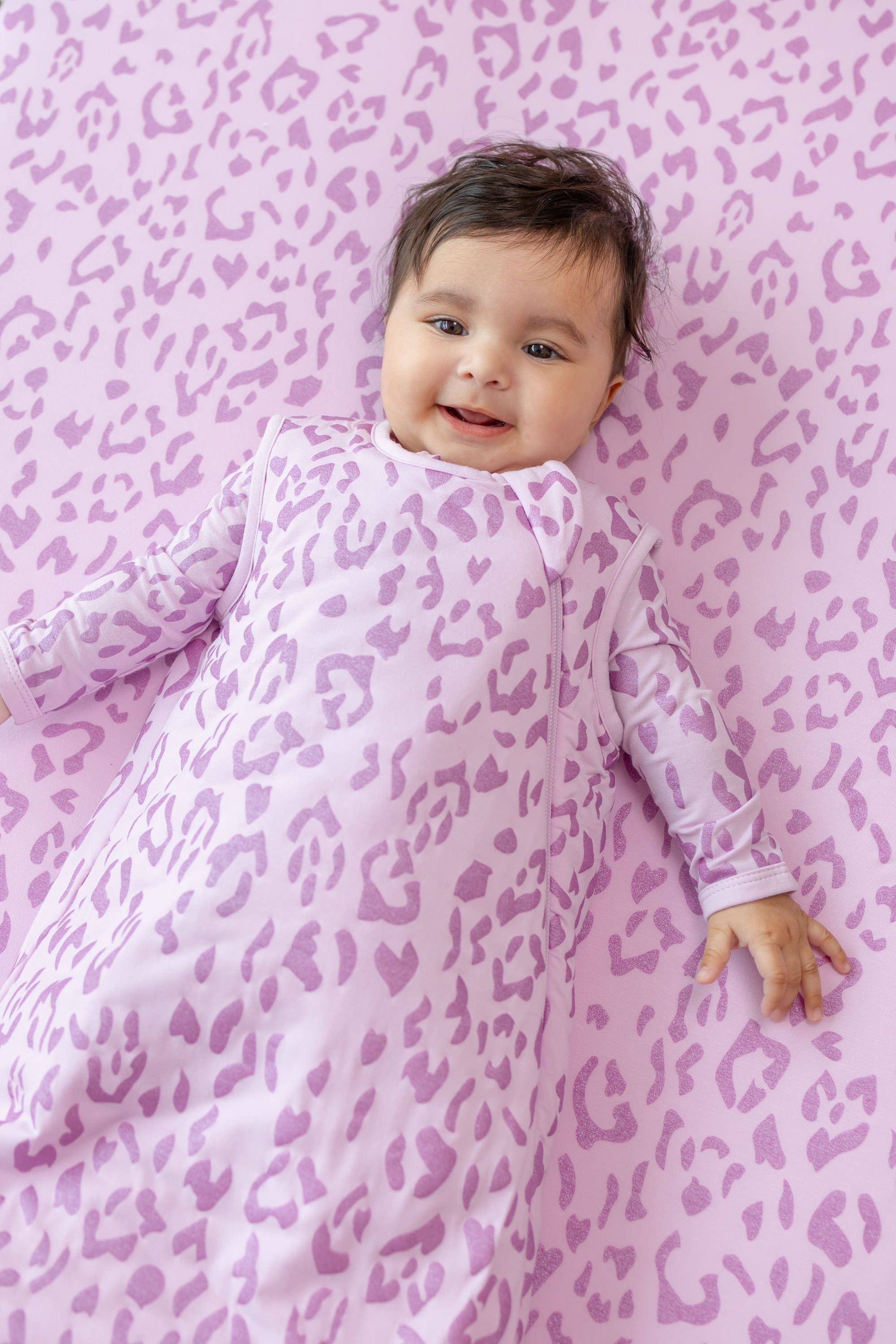 Baby in Thistle Leopard print sleep bag lying on a similar print sheet
