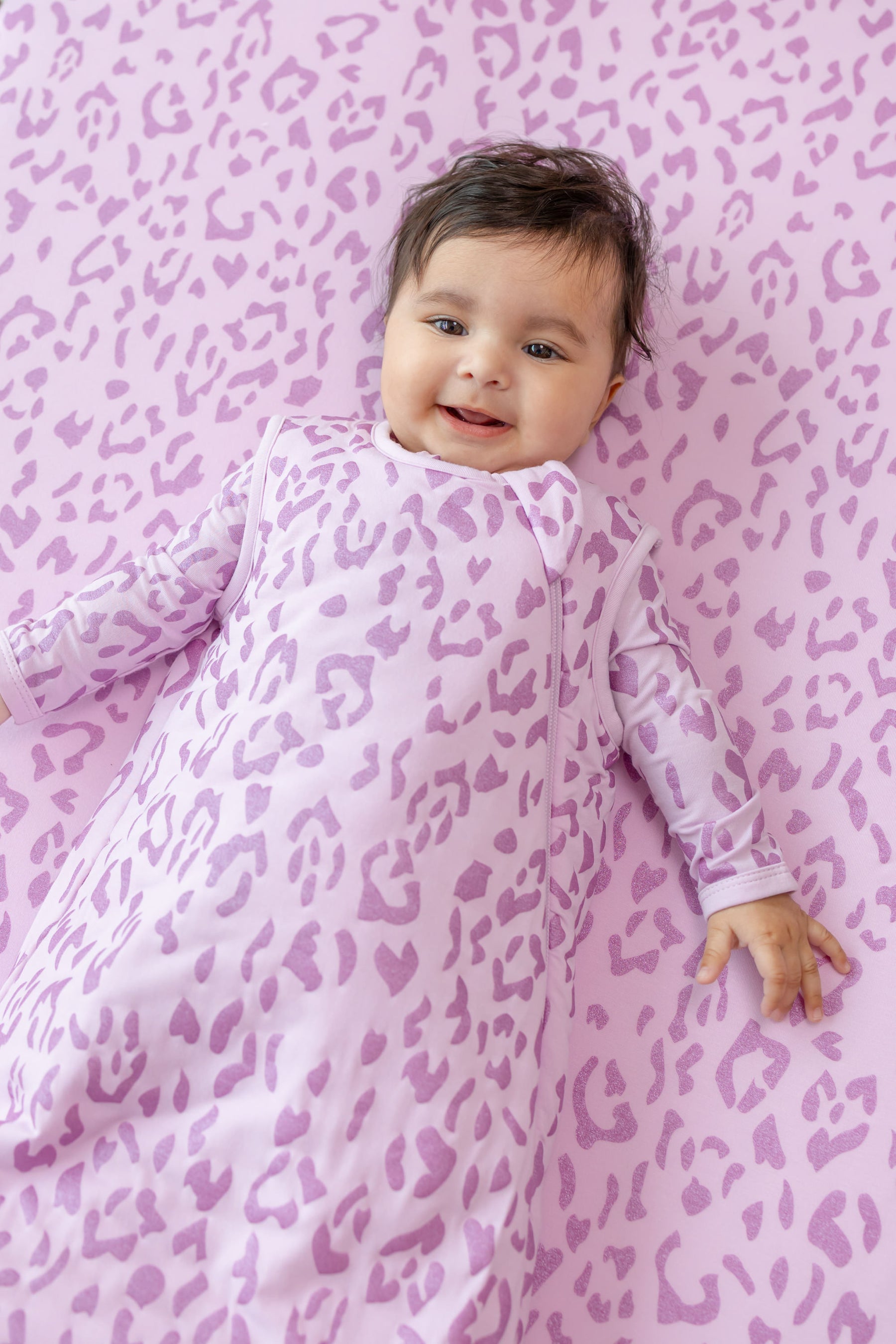 Baby in Thistle Leopard print sleep bag lying on a similar print sheet