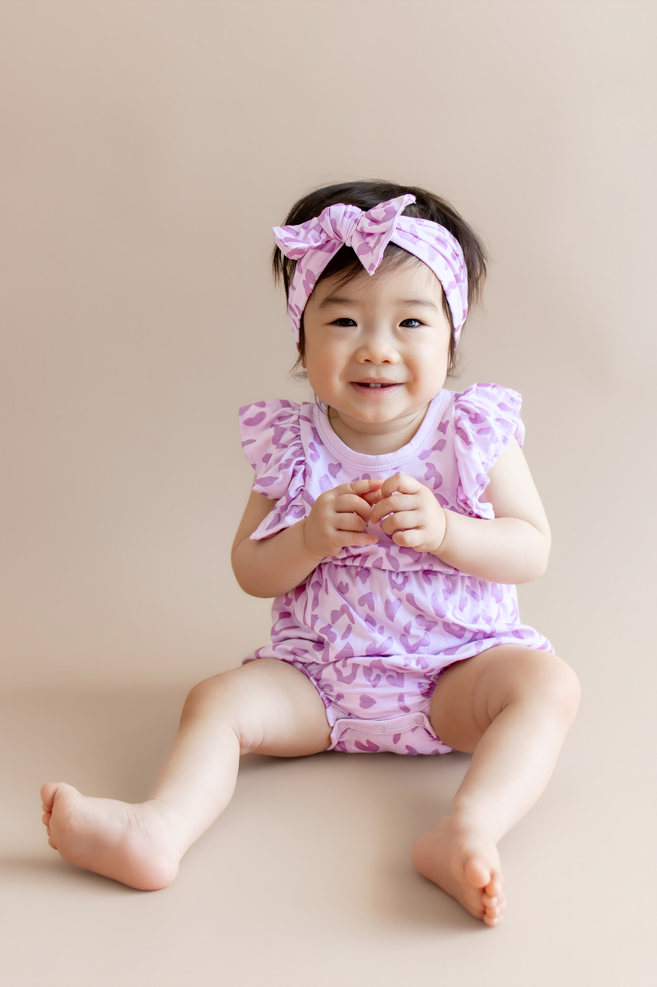 Baby wearing a Thistle Leopard print Bubble romper and bow headband on a beige background