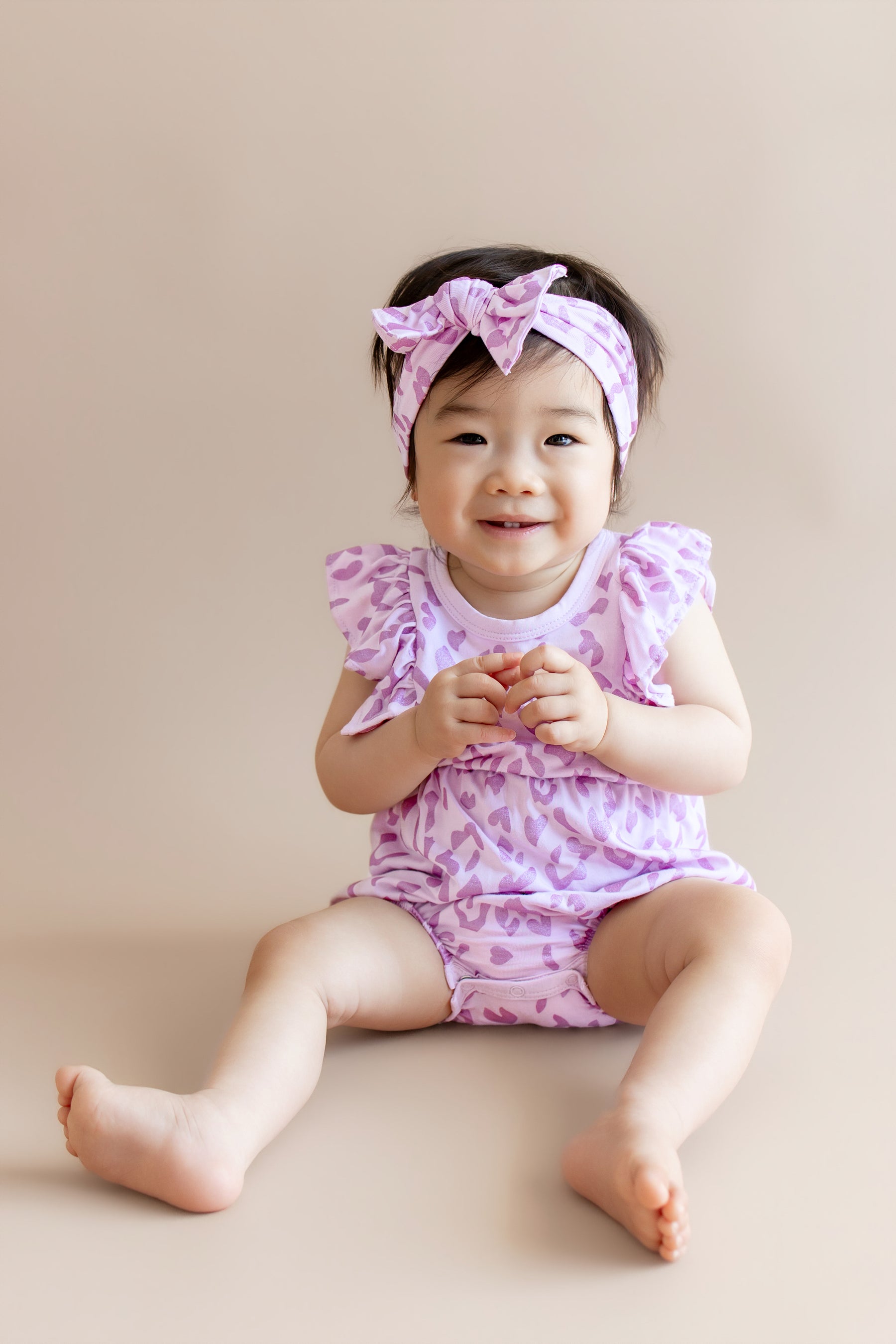 Baby wearing a Thistle Leopard print Bubble romper and bow headband on a beige background