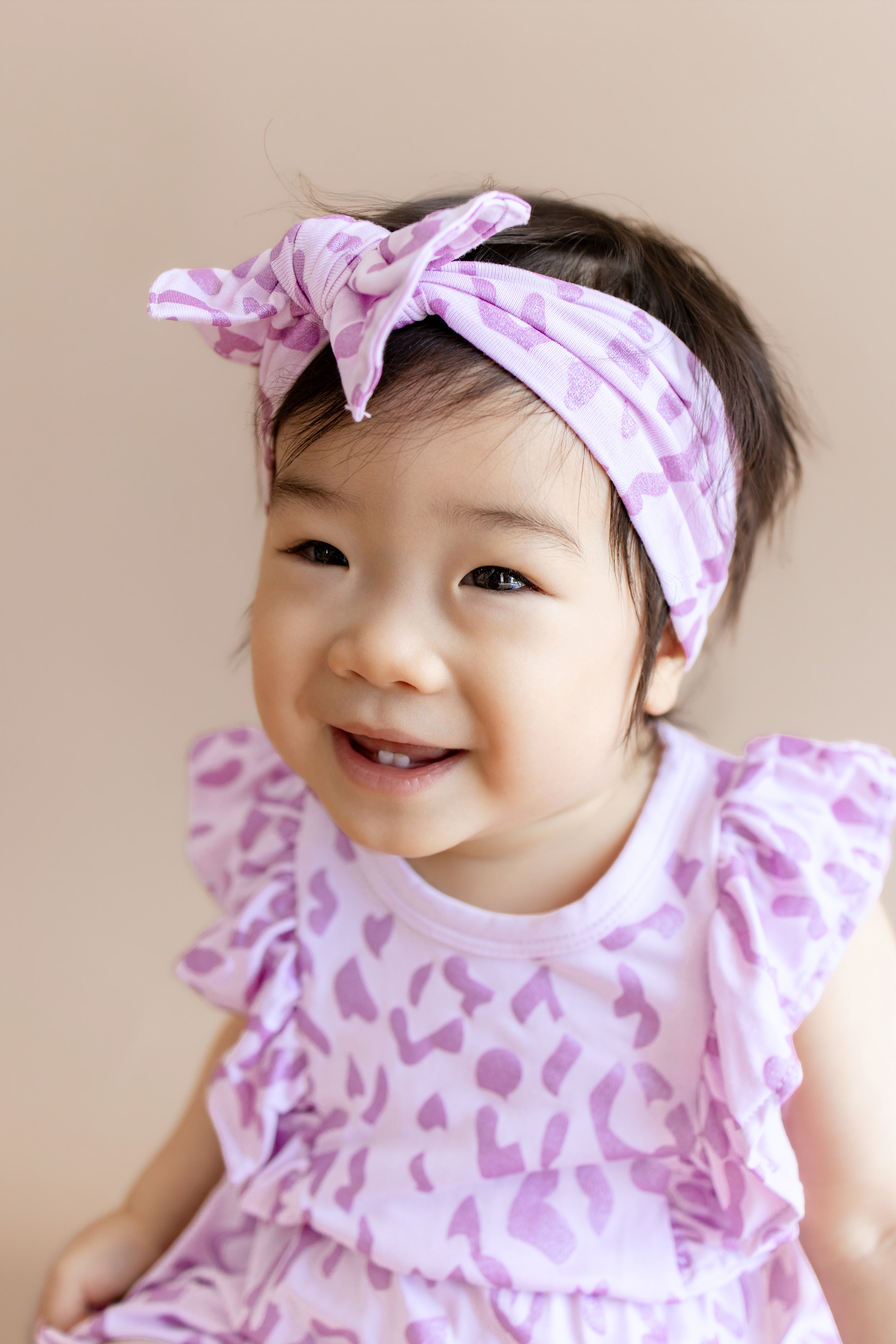 Baby wearing a Thistle Leopard print Bubble romper and bow headband on a beige background