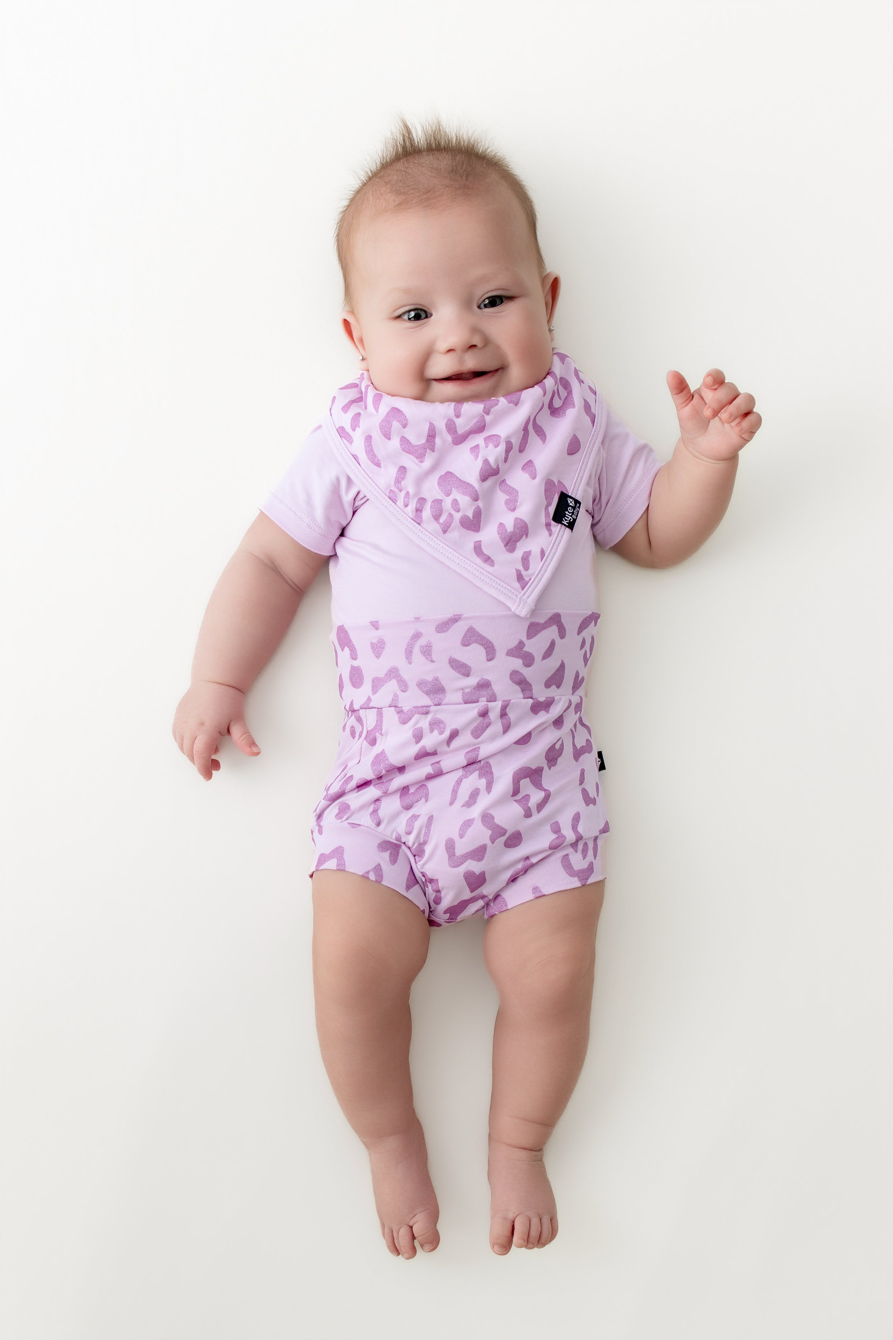 Baby wearing a Thistle Leopard print Bummies and bib over a thistle bodysuit on a beige background