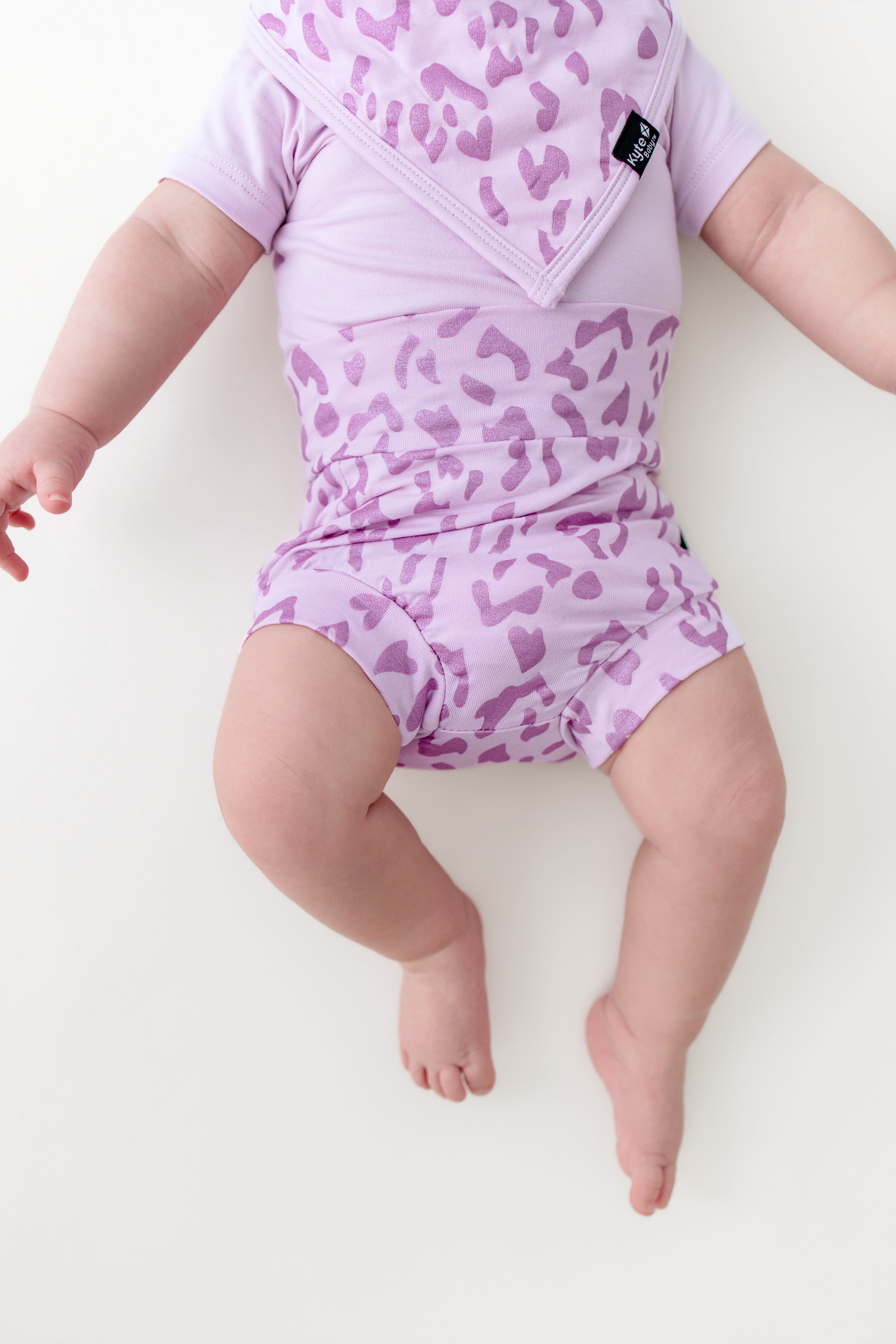 Baby wearing a Thistle Leopard print Bummies and bib over a thistle bodysuit on a beige background