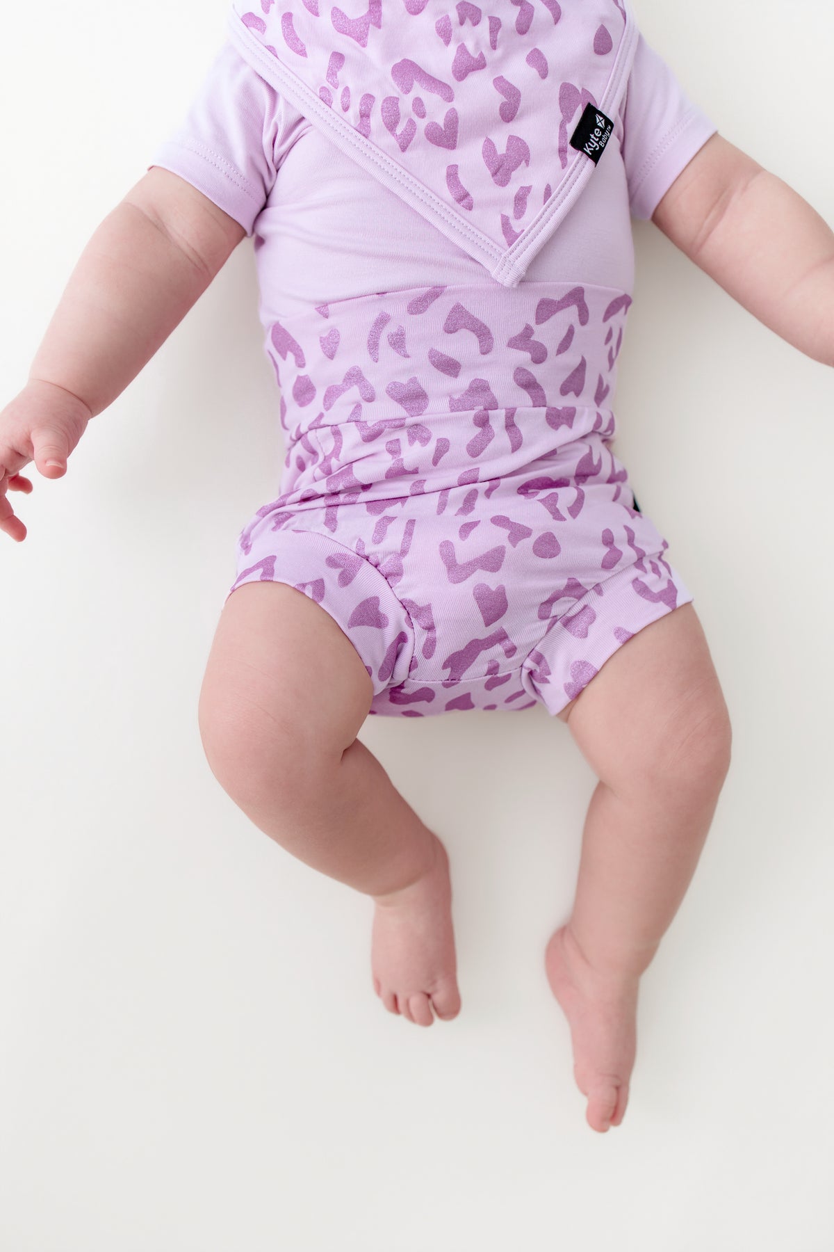 Baby wearing a Thistle Leopard print Bummies and bib over a thistle bodysuit on a beige background