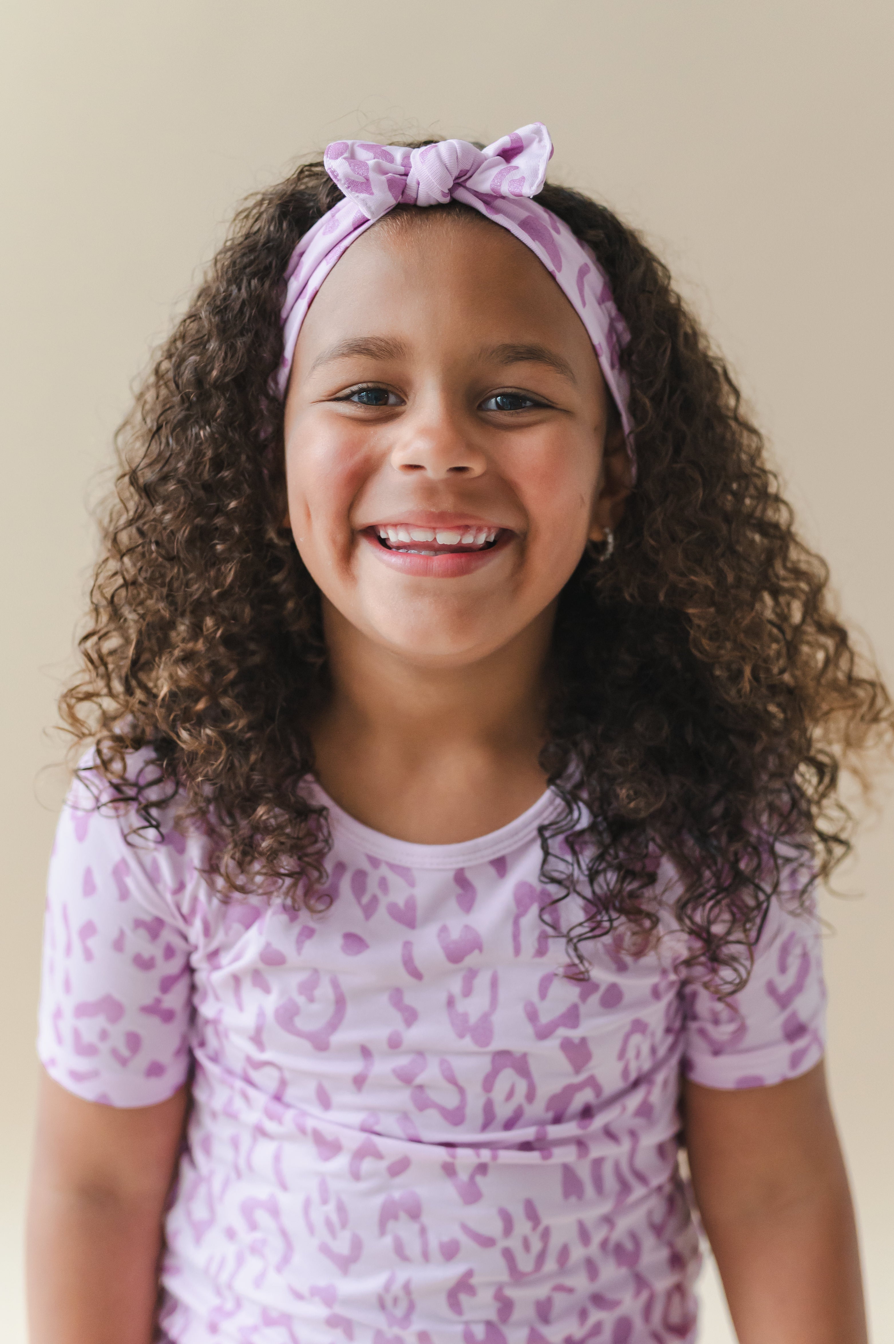 Child wearing a Thistle Leopard print Knotted Bow headband and shirt on a beige background
