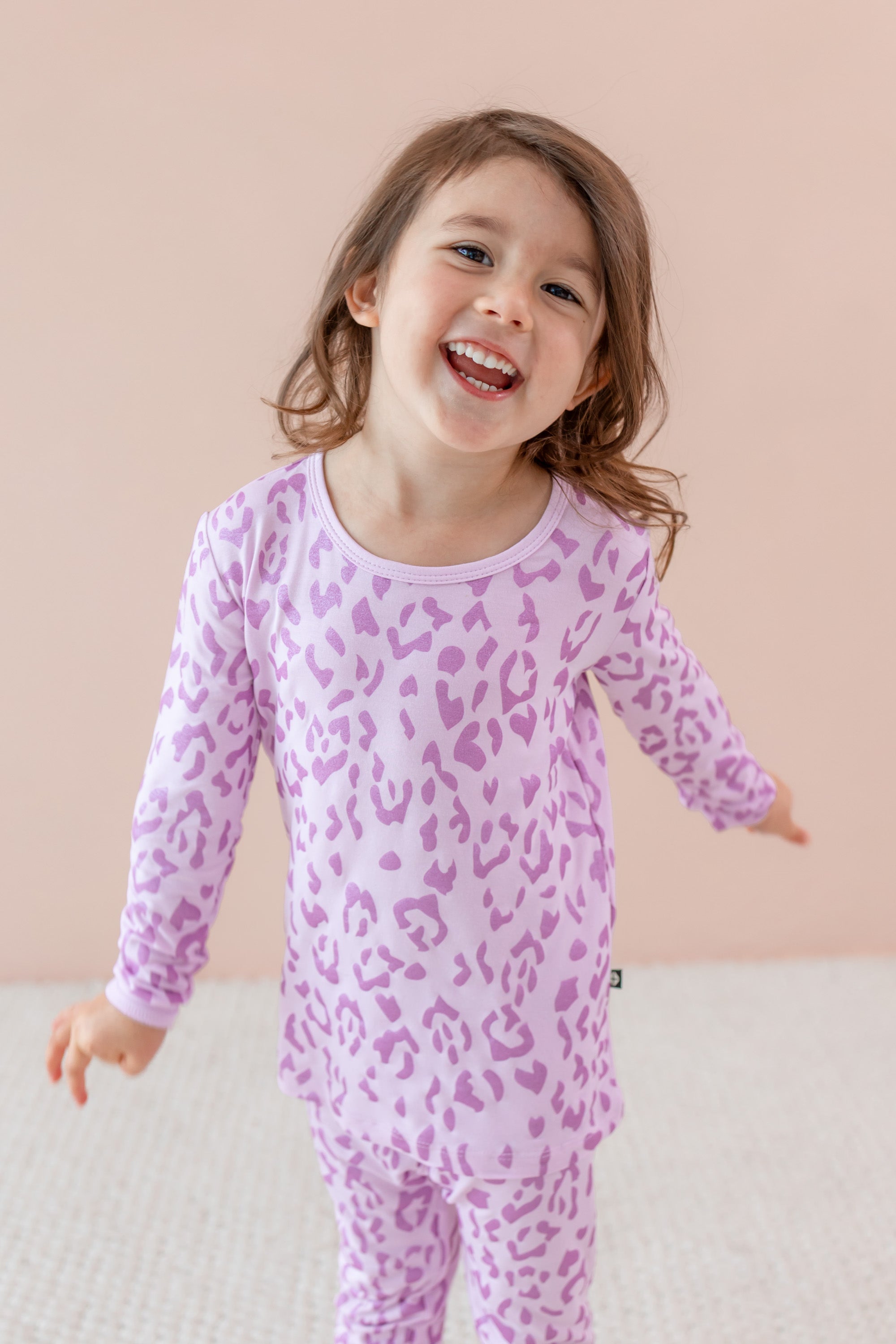 Child smiling in Long sleeve pajama set in Thistle Leopard print on a beige background