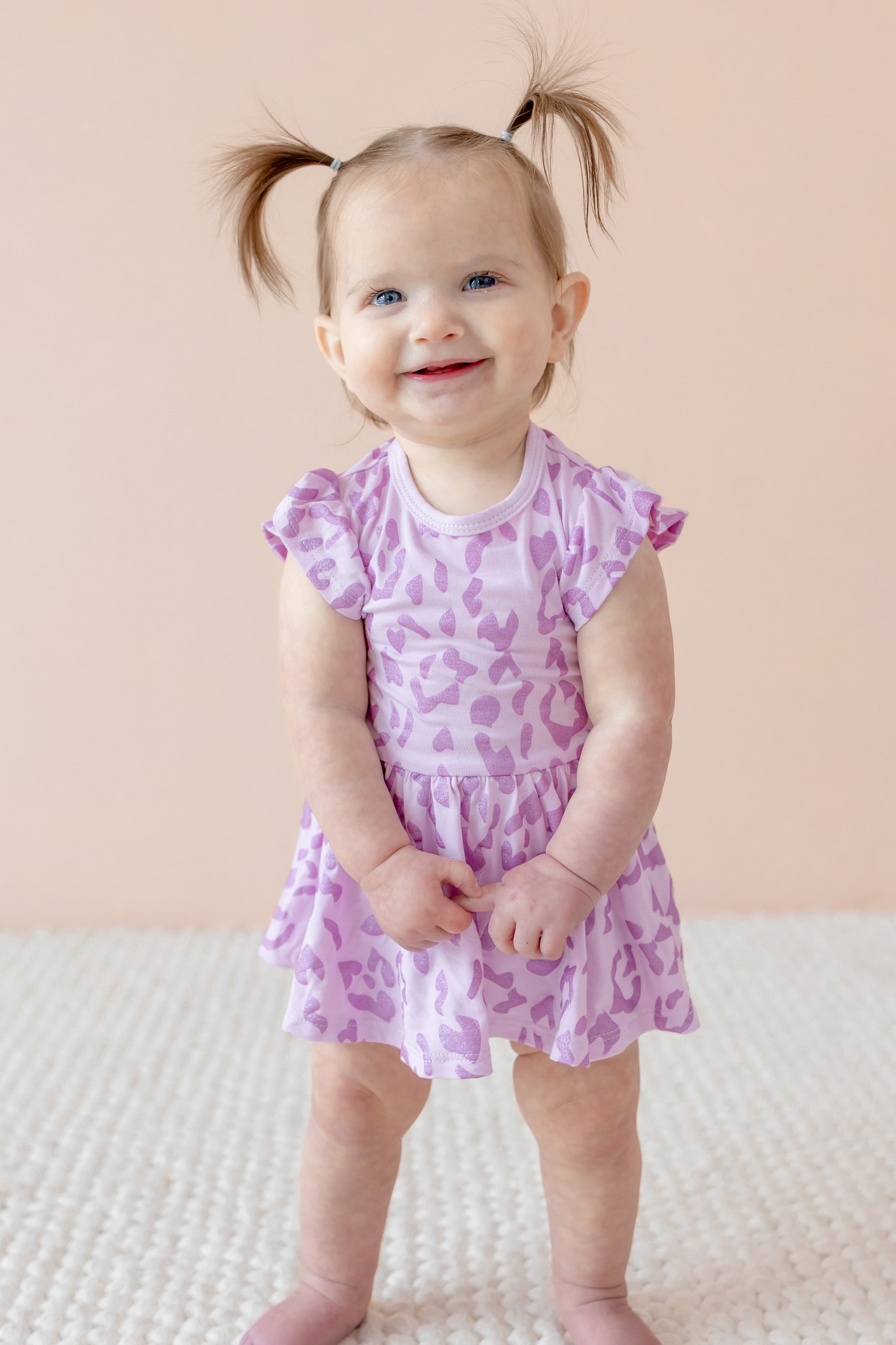 Child wearing Twirl bodysuit dress in Thistle Leopard print on a beige background