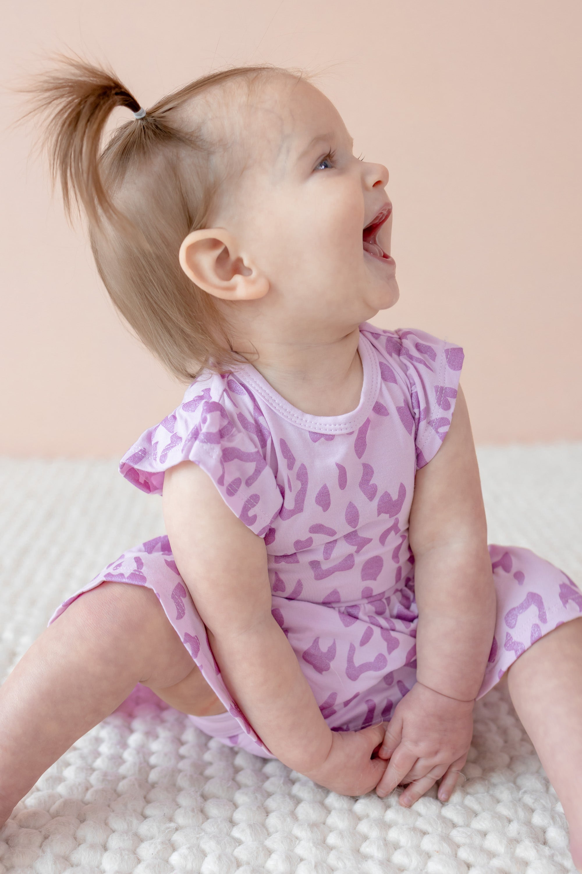 Child sitting in Twirl bodysuit dress in Thistle Leopard print on a beige background