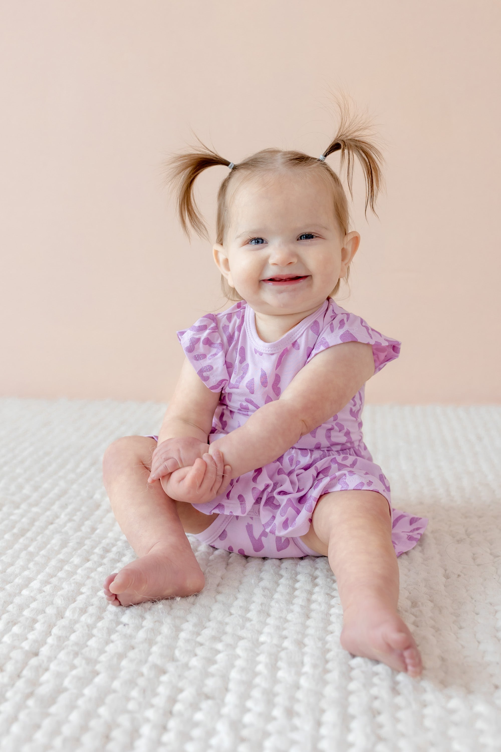 Child smiling in Twirl bodysuit dress in Thistle Leopard print on a beige background